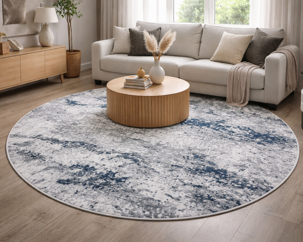 Tapete redondo cinza e azul em sala com mesa de madeira, sofá cinza e almofadas