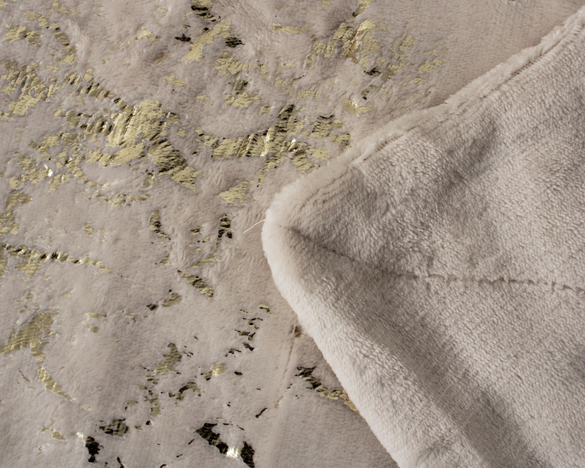 Cobertor bege felpudo com padrão dourado e detalhe do verso macio.