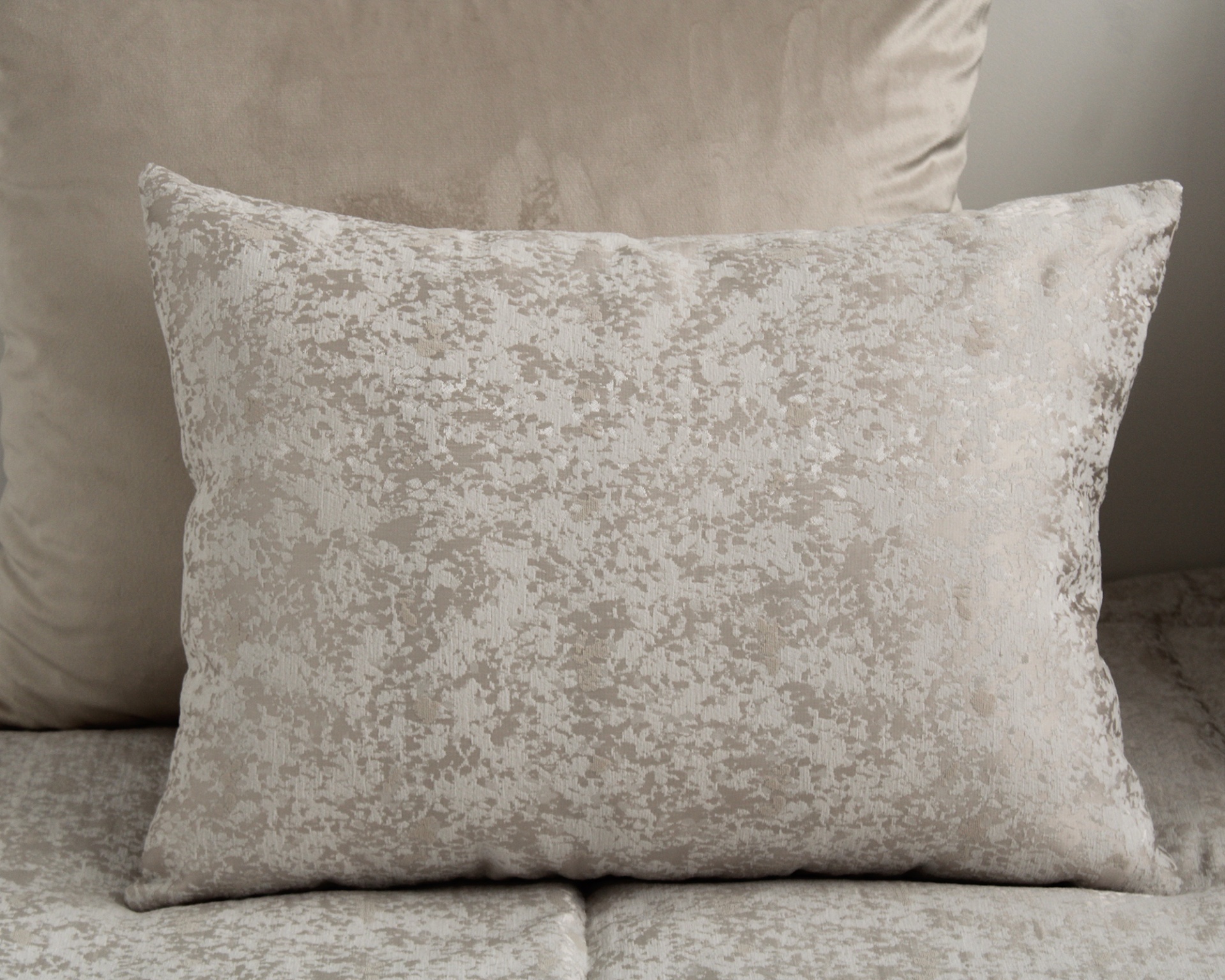 Almofada rectangular bege com padrão texturizado sobre sofá bege.