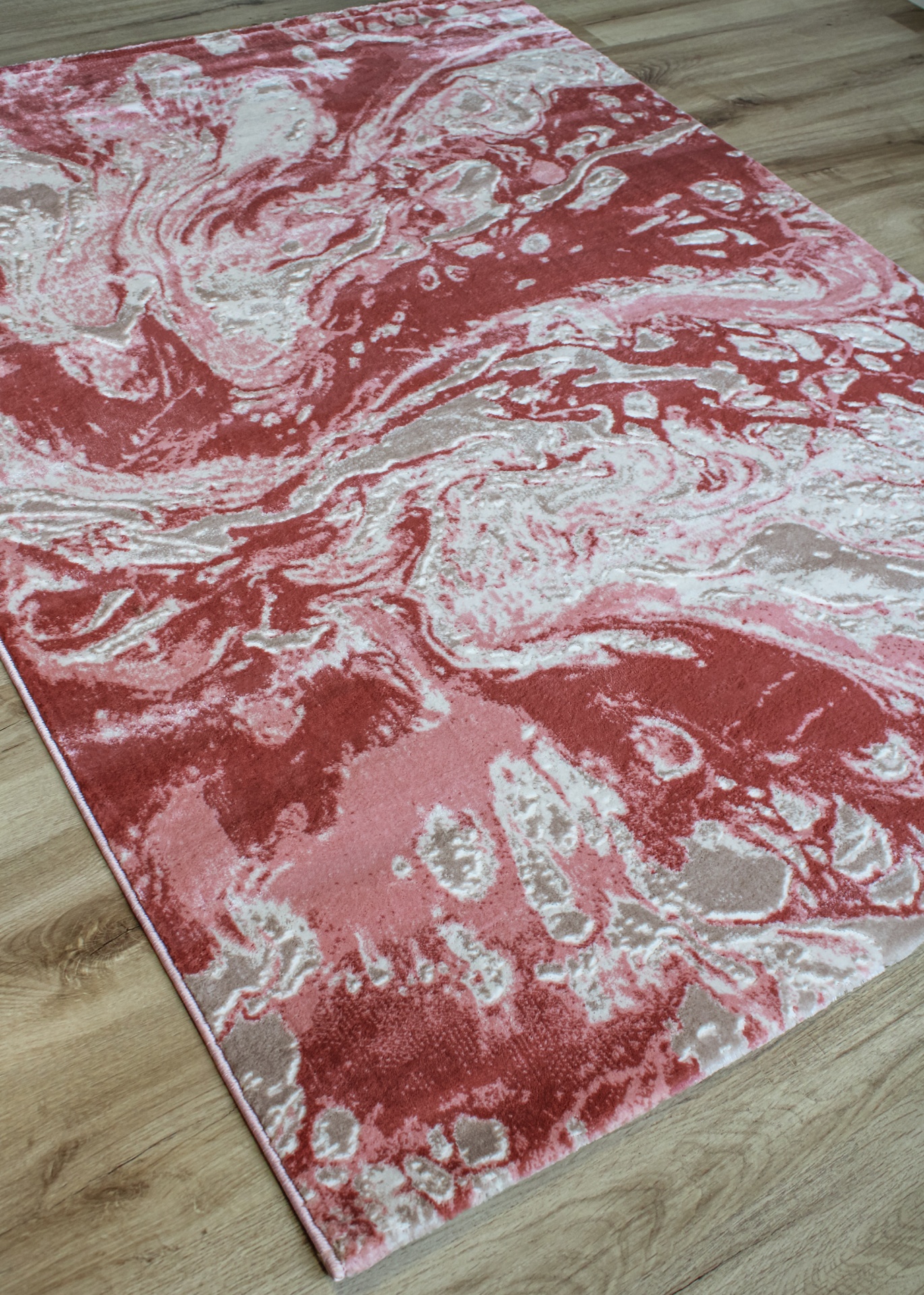 Tapete decorativo abstrato em tons vermelhos e rosa sobre chão de madeira