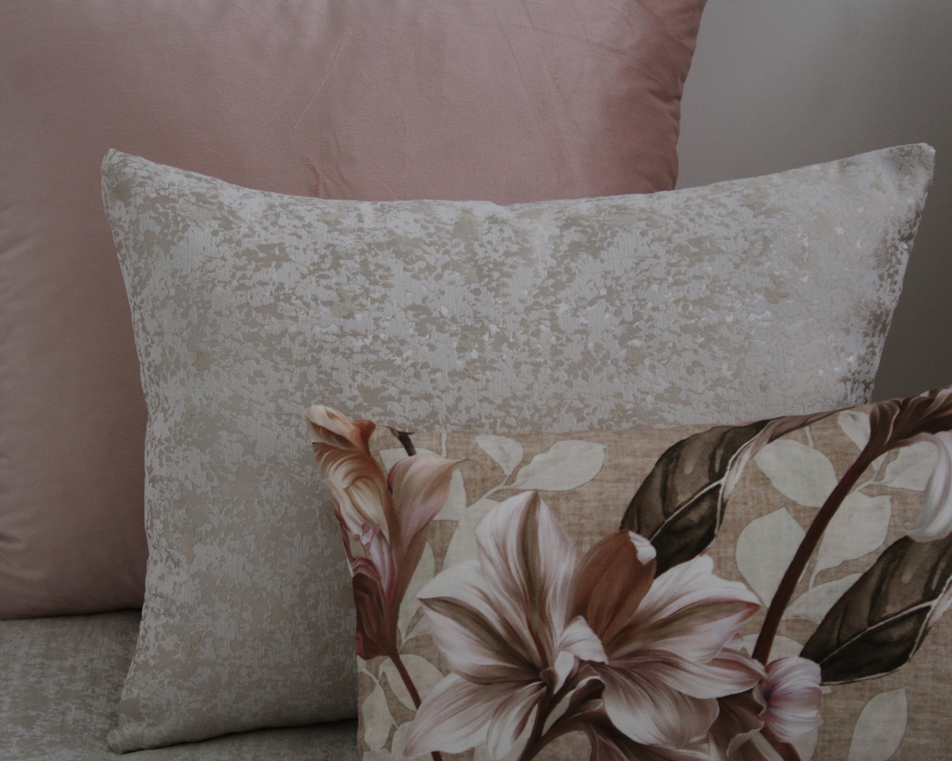 Almofadas decorativas rosa, cinza com textura e floral castanho no sofá cinza.