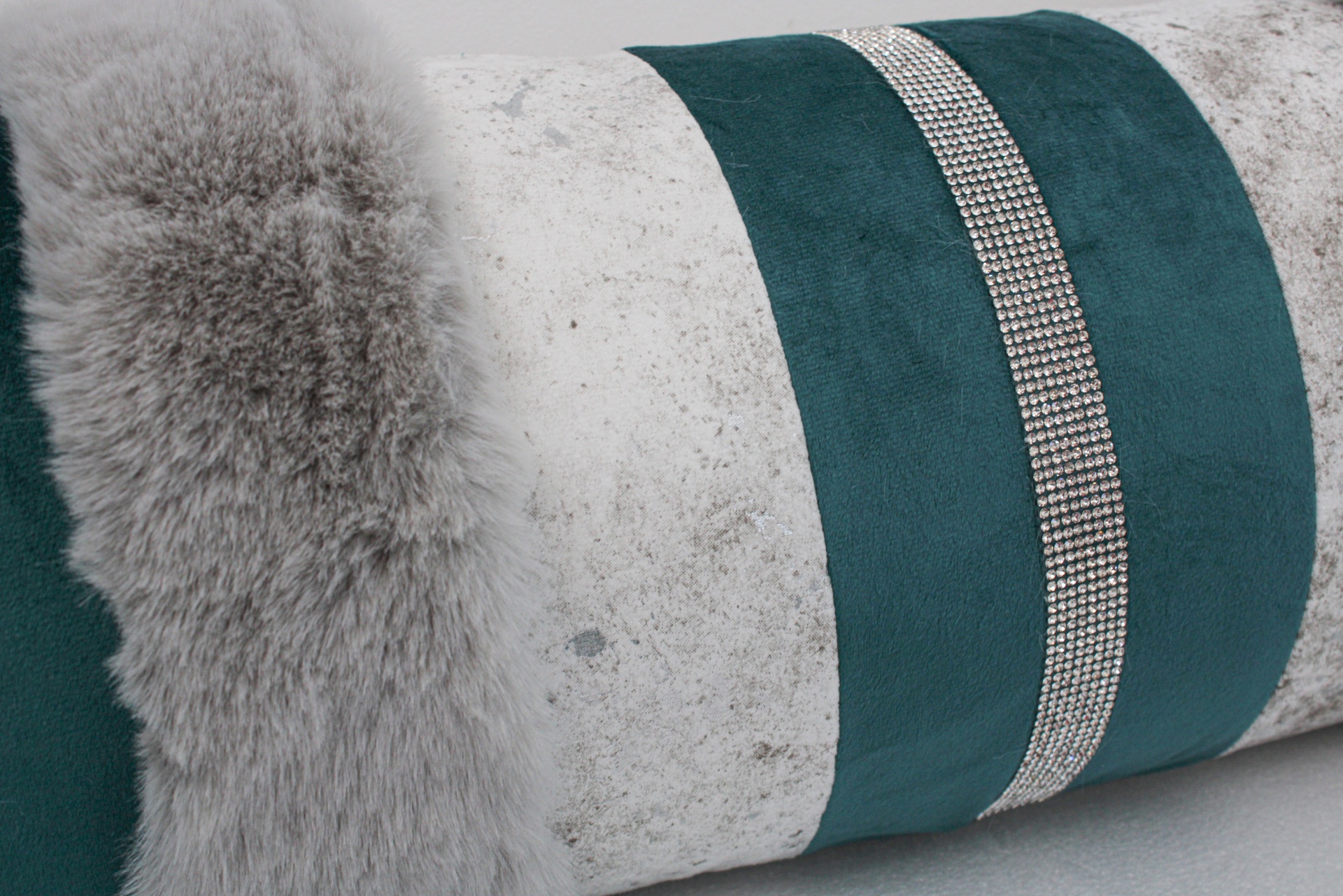 Almofada rolão cinzenta e verde com faixa de pedras brilhantes e borda de pelo