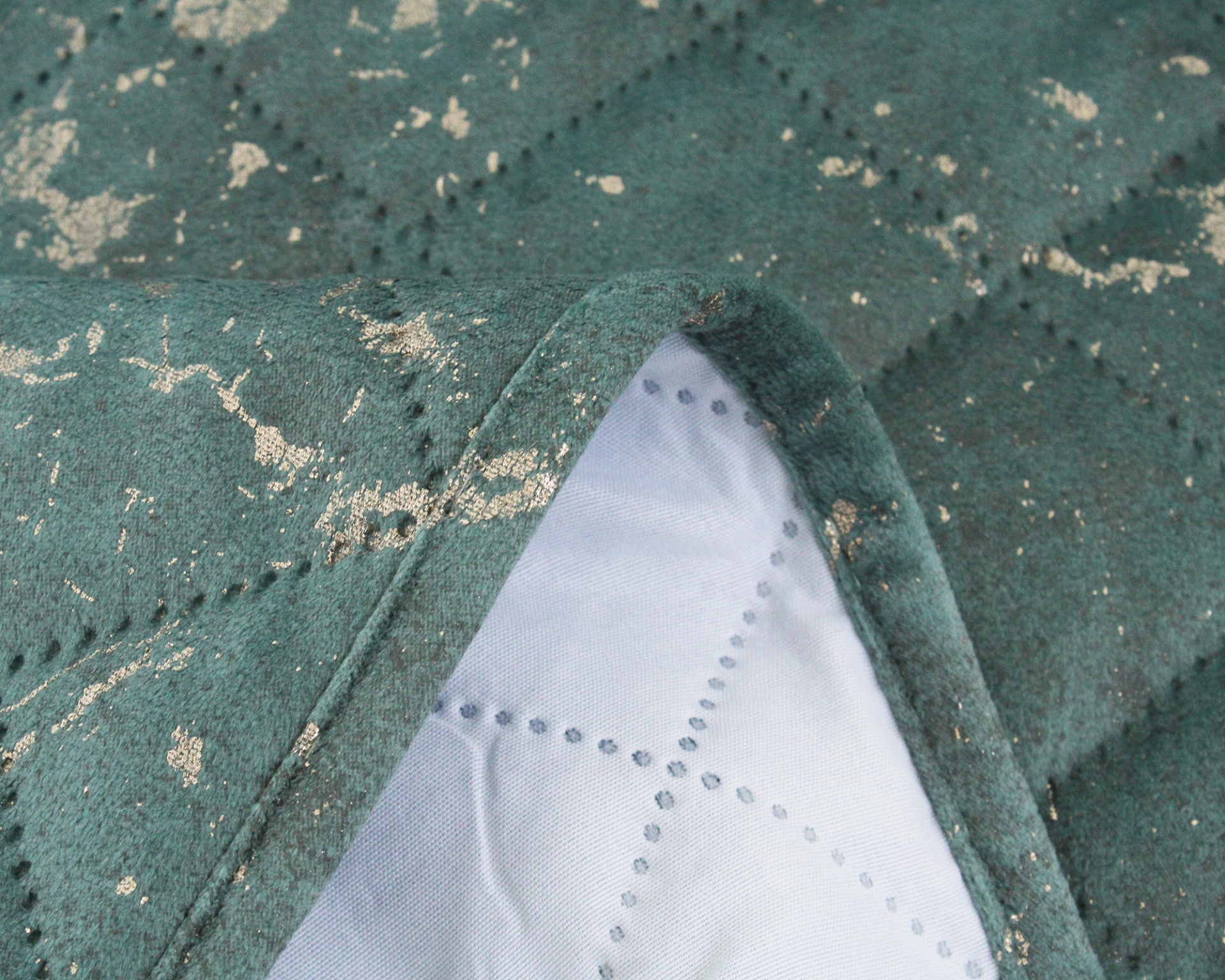 Tecido verde com manchas douradas e costura bordada com recorte mostrando tecido branco com pontos azuis