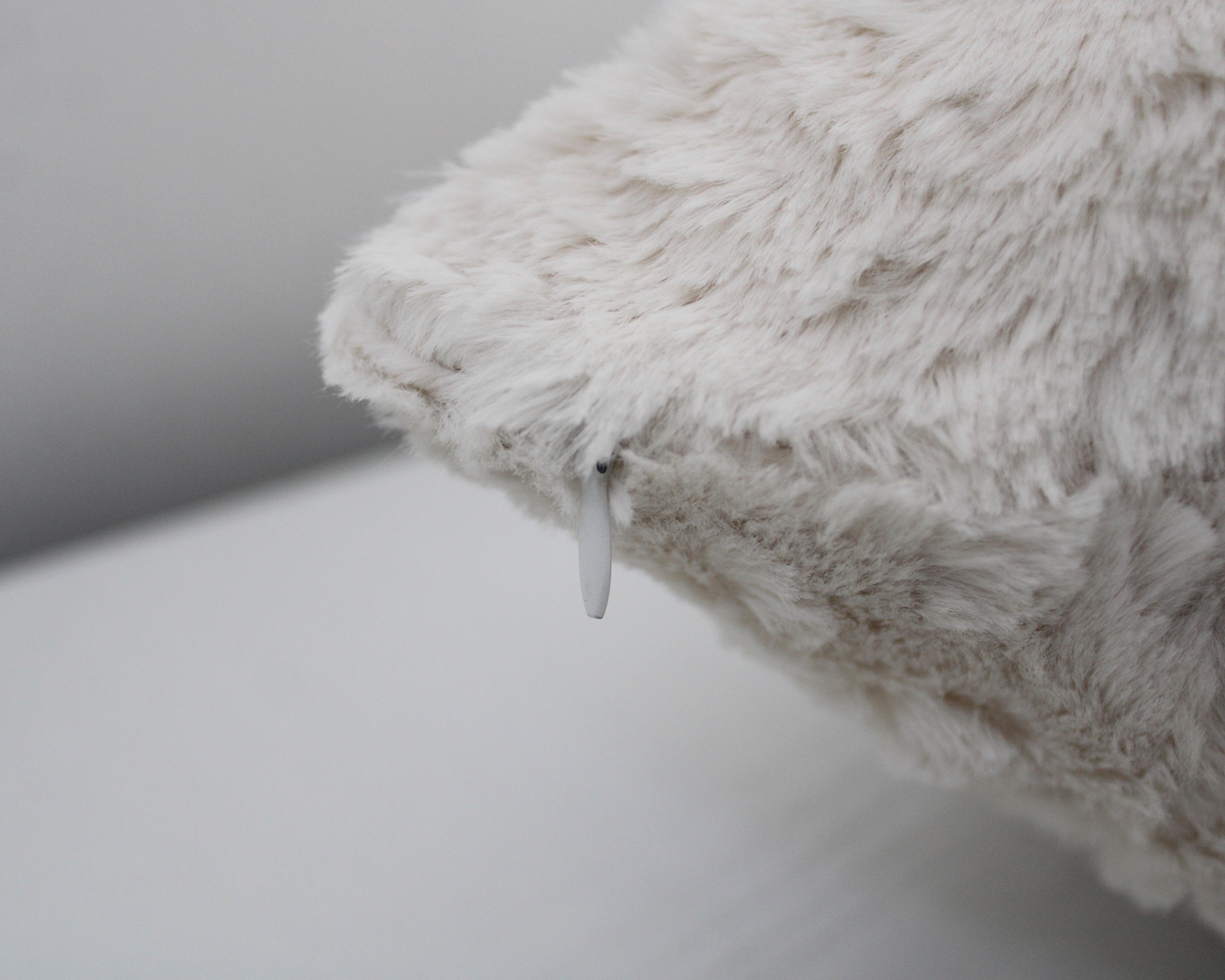 Almofada de pelo sintético branco-creme com etiqueta