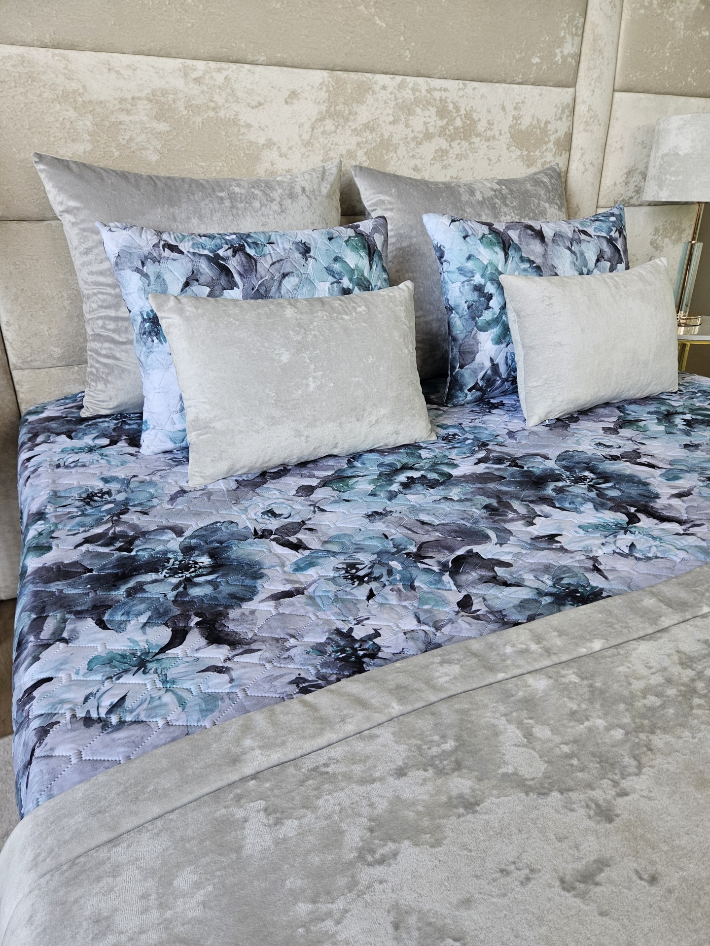 Cama com colcha e almofadas decorativas em padrão floral azul e veludo cinza