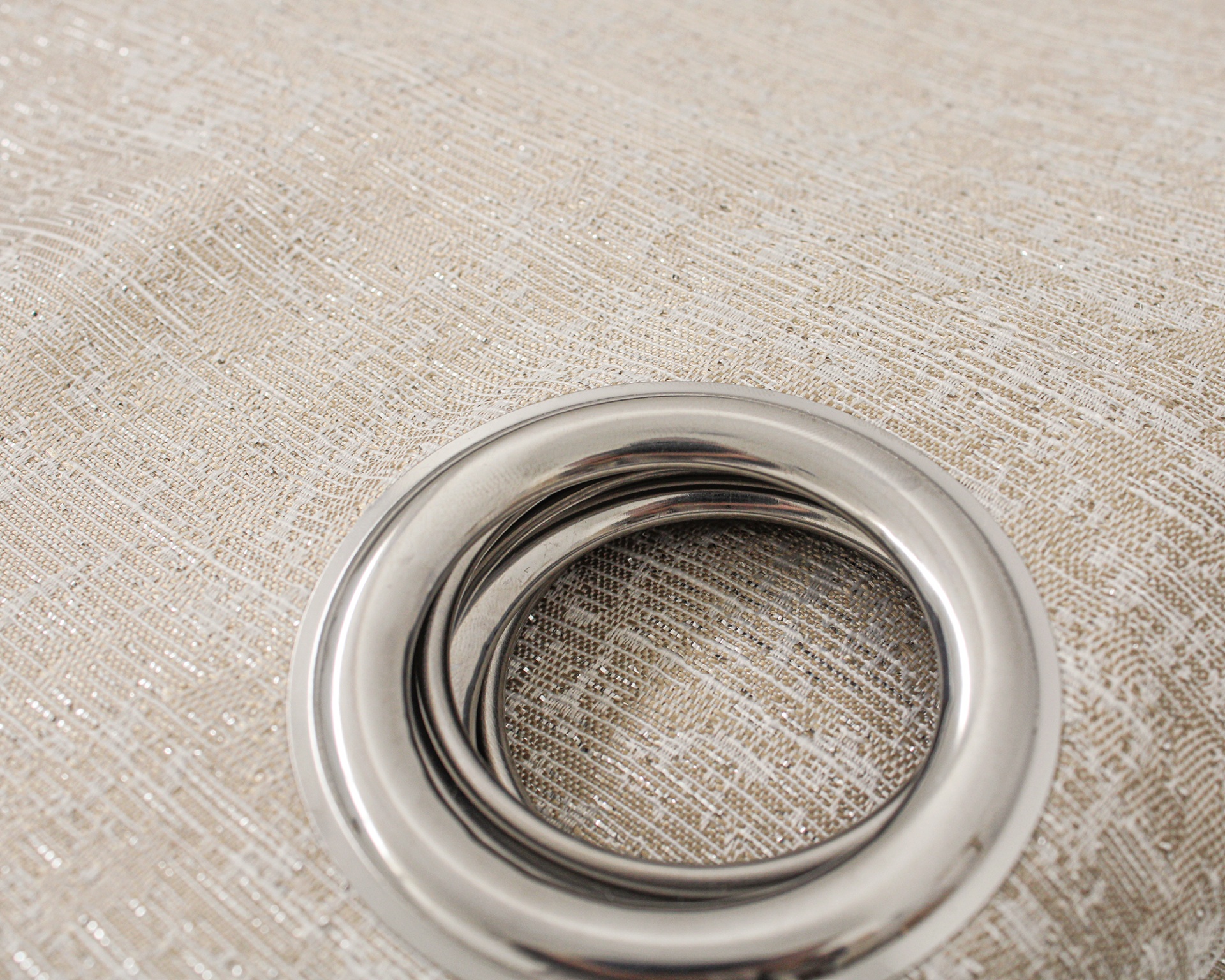 Anel metálico prateado sobre tecido bege texturizado