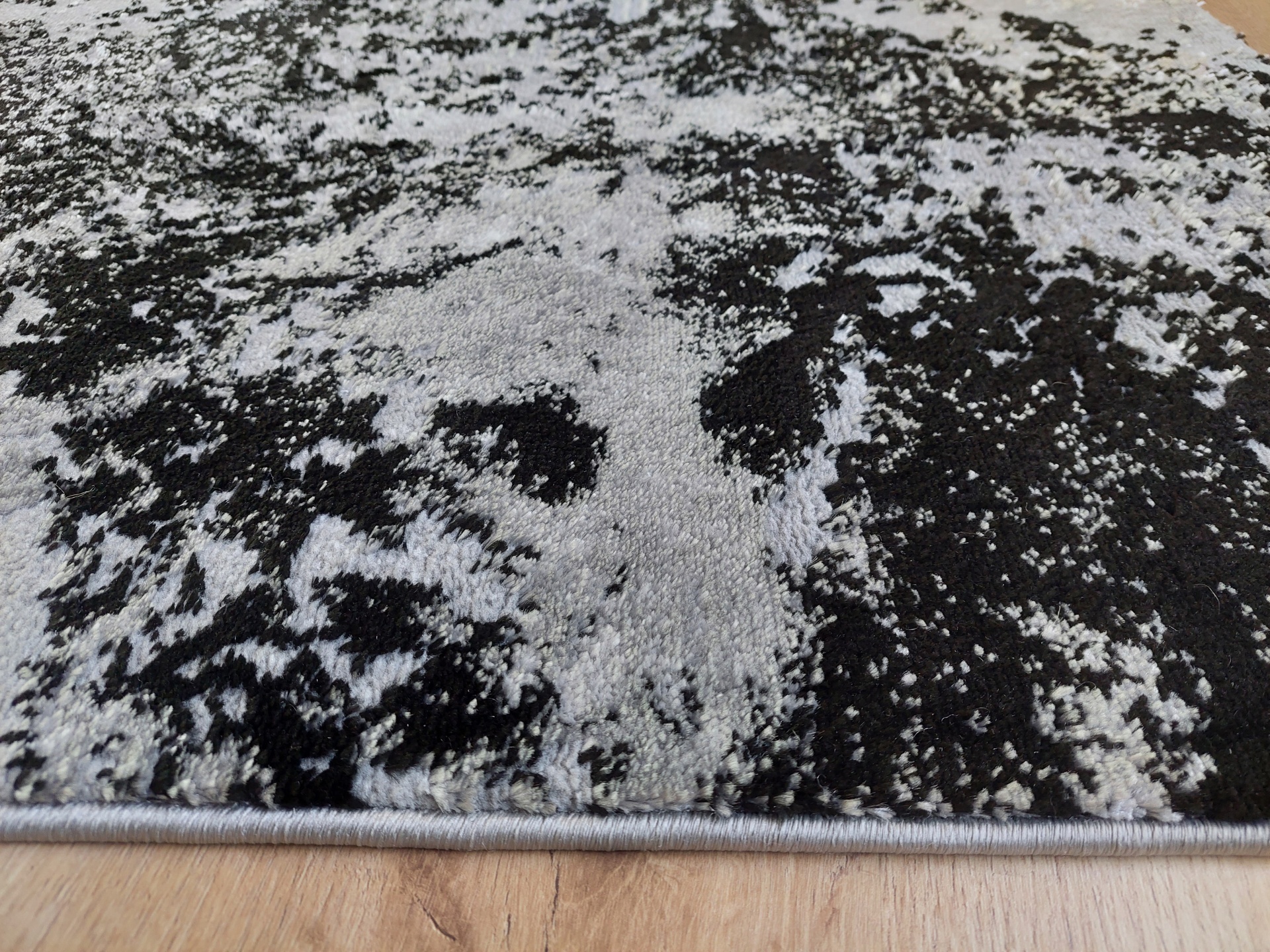 Tapete cinzento e preto com padrão abstracto sobre chão de madeira