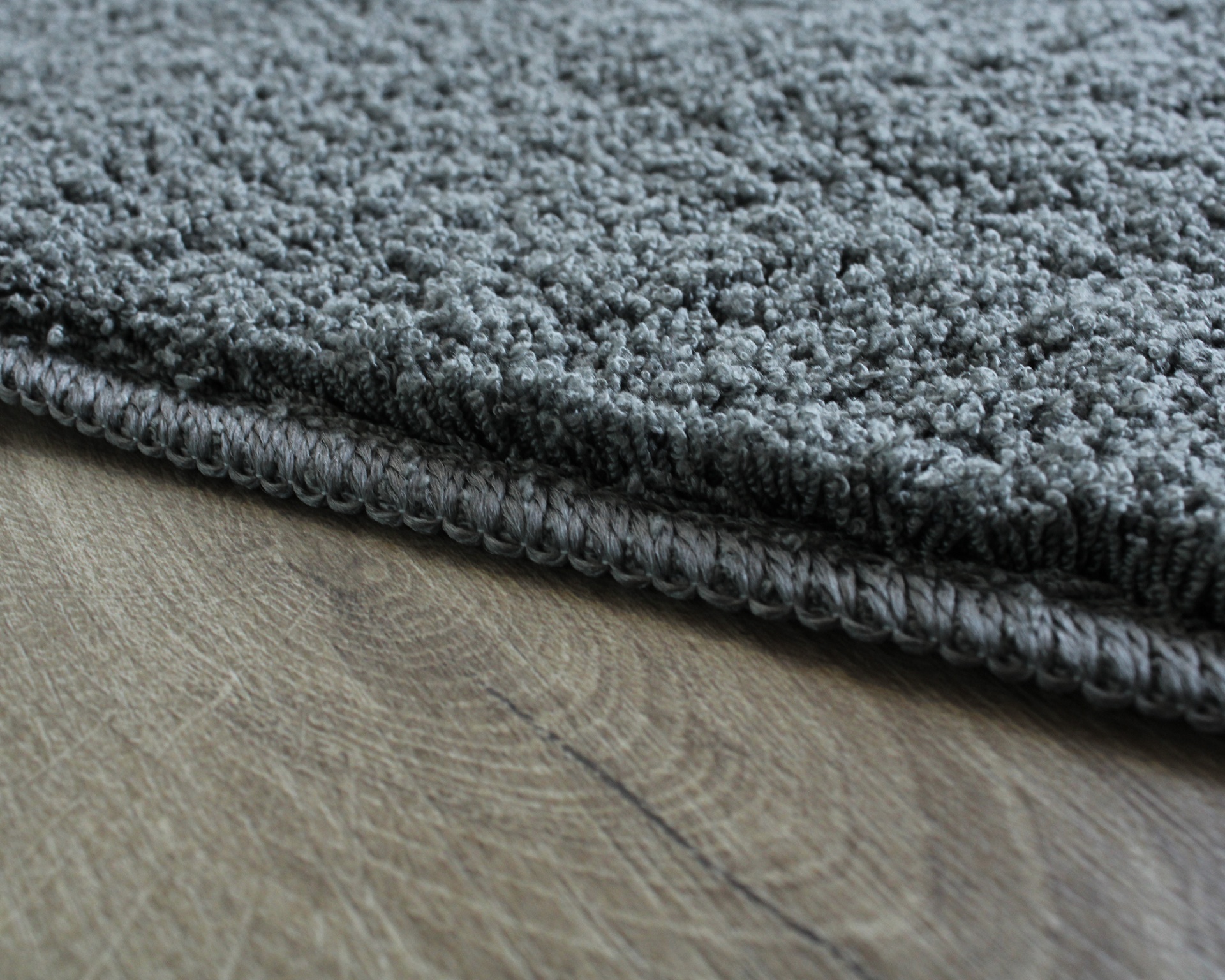 Tapete cinzento felpudo com borda costurada sobre chão de madeira clara