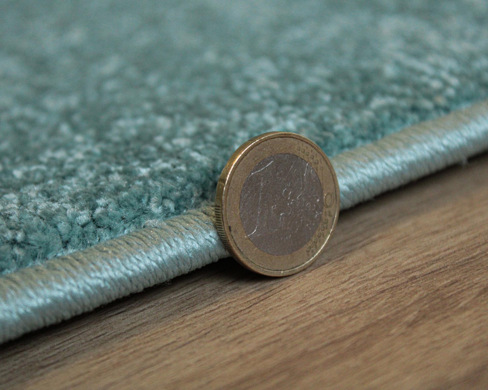 Tapete azul claro com textura felpuda e moeda de 1 euro encostada para comparação.