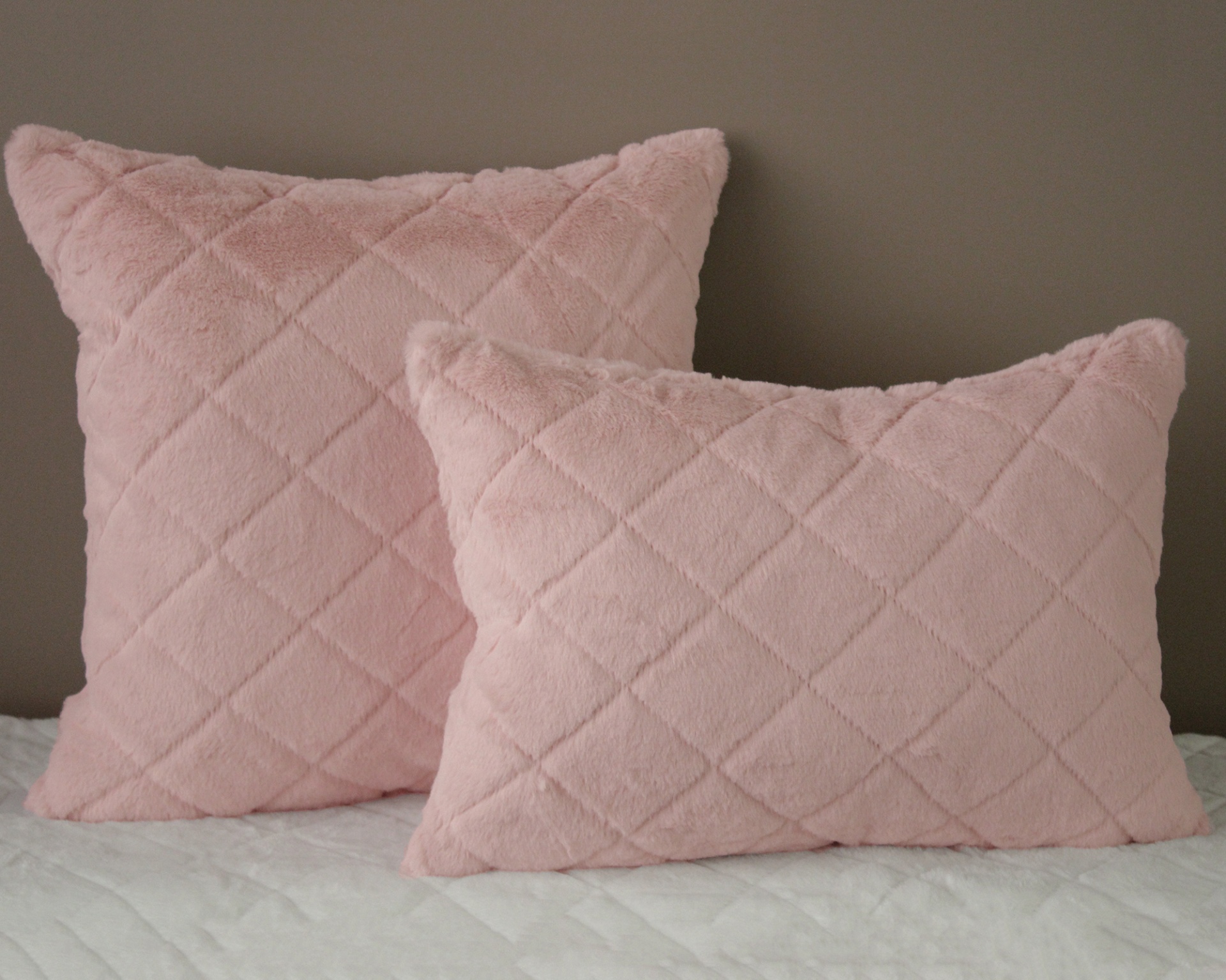 Duas almofadas rosa claro acolchoadas em losango numa cama