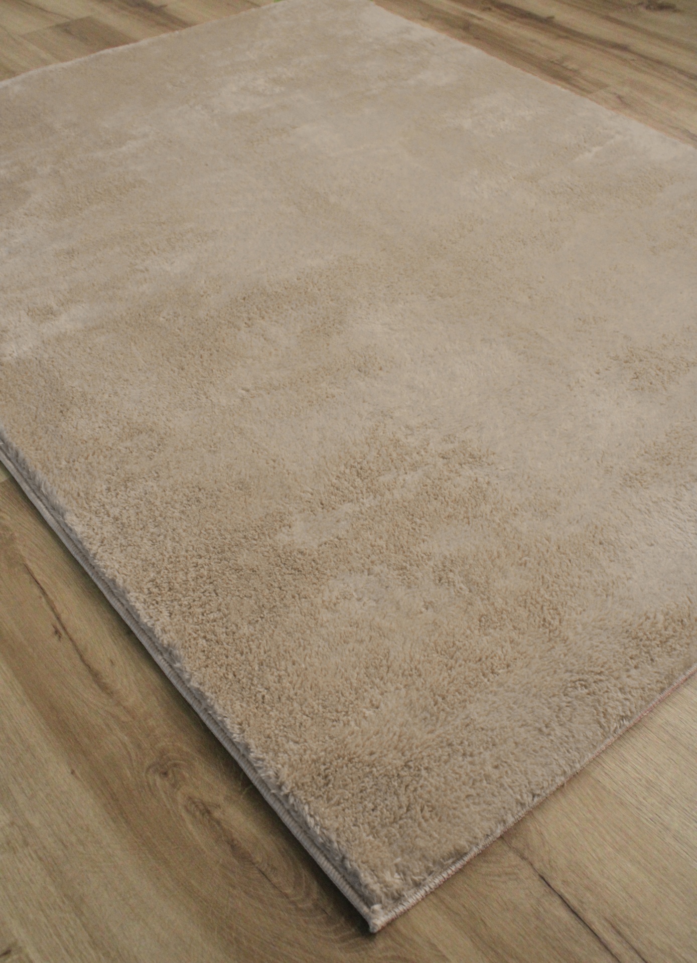 Tapete bege claro felpudo sobre chão de madeira clara.