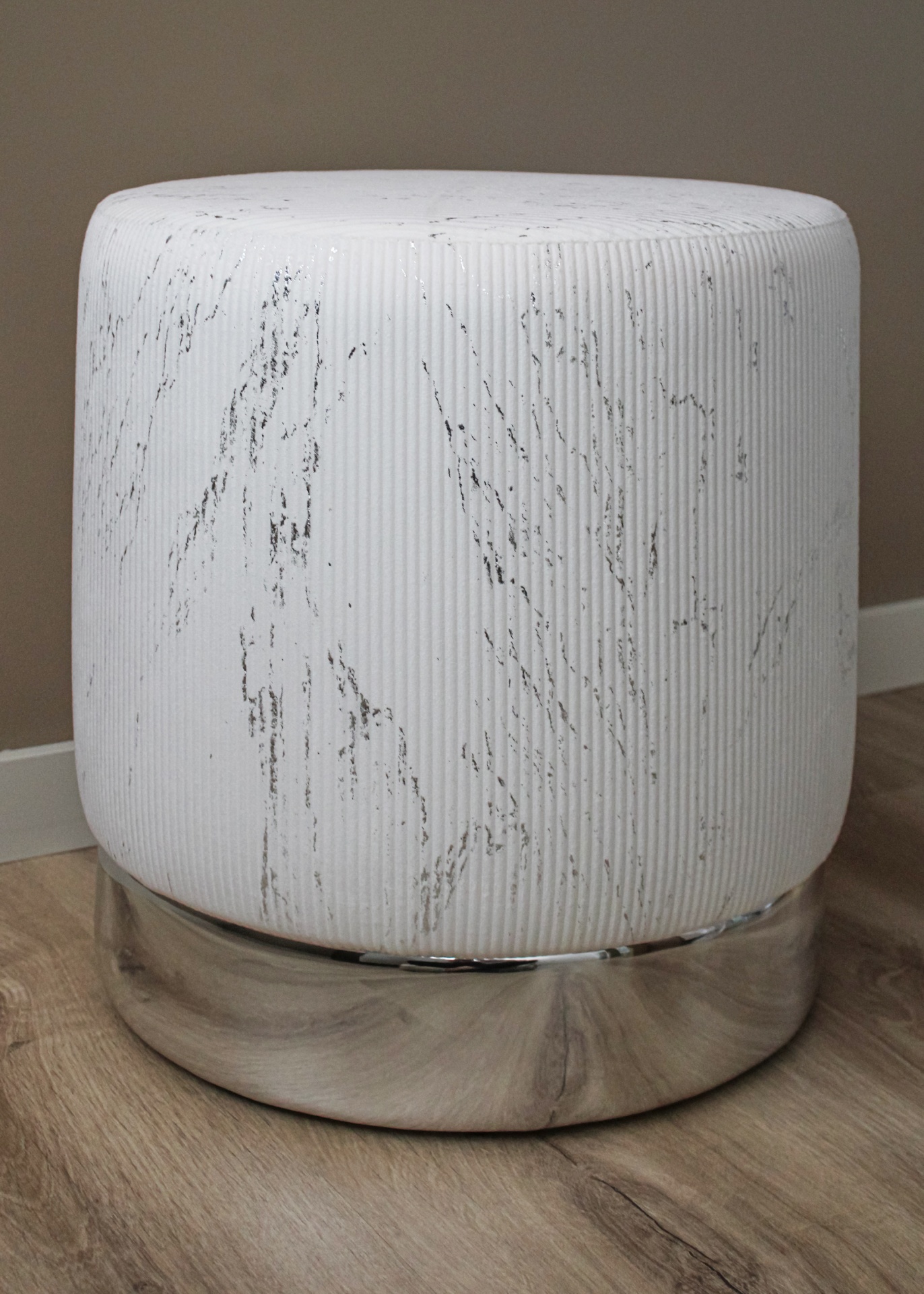 Pufe redondo branco com padrão marmoreado e base cromada sobre chão de madeira clara