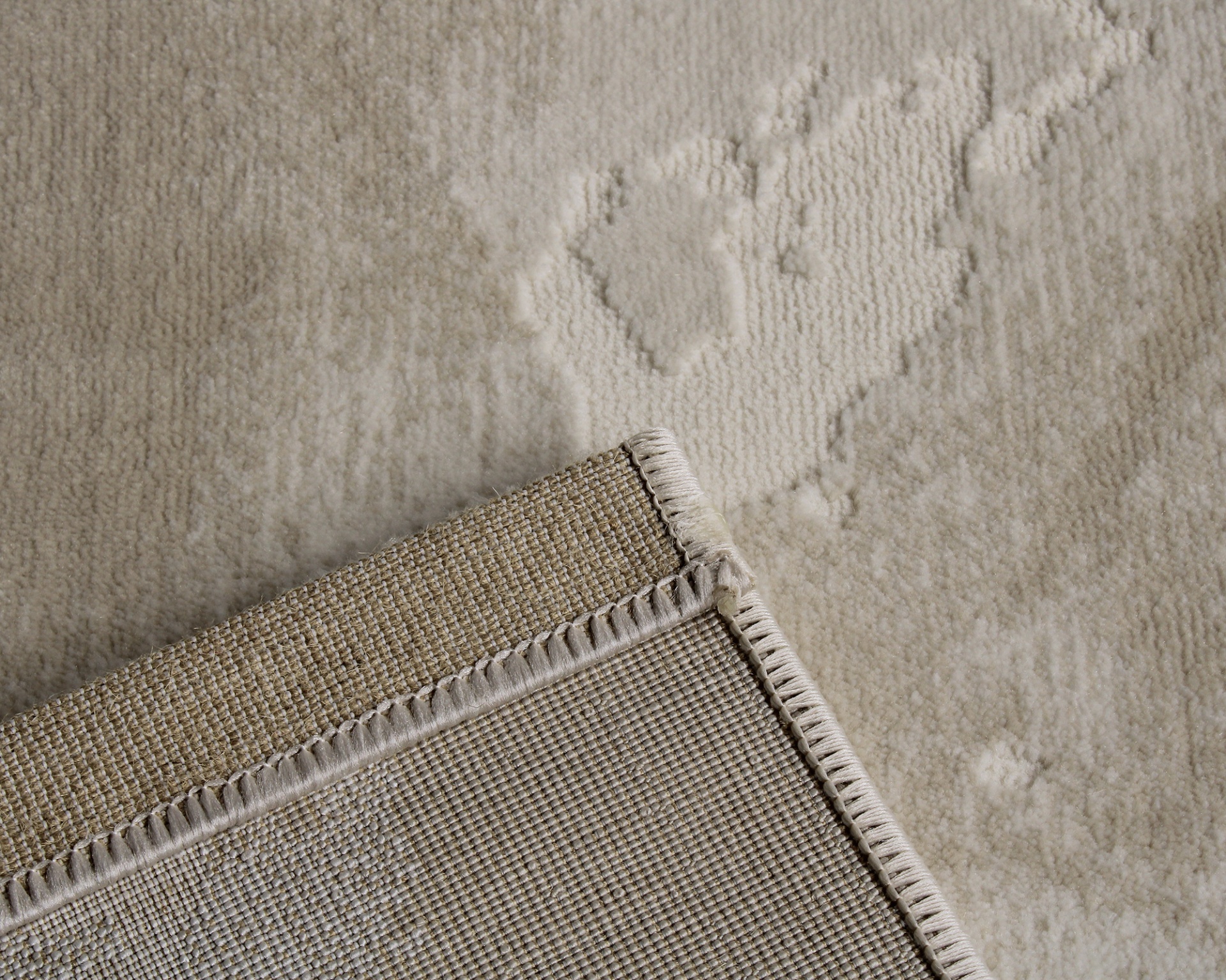 Tapete bege claro com padrão em relevo e canto virado que mostra a trama tecida