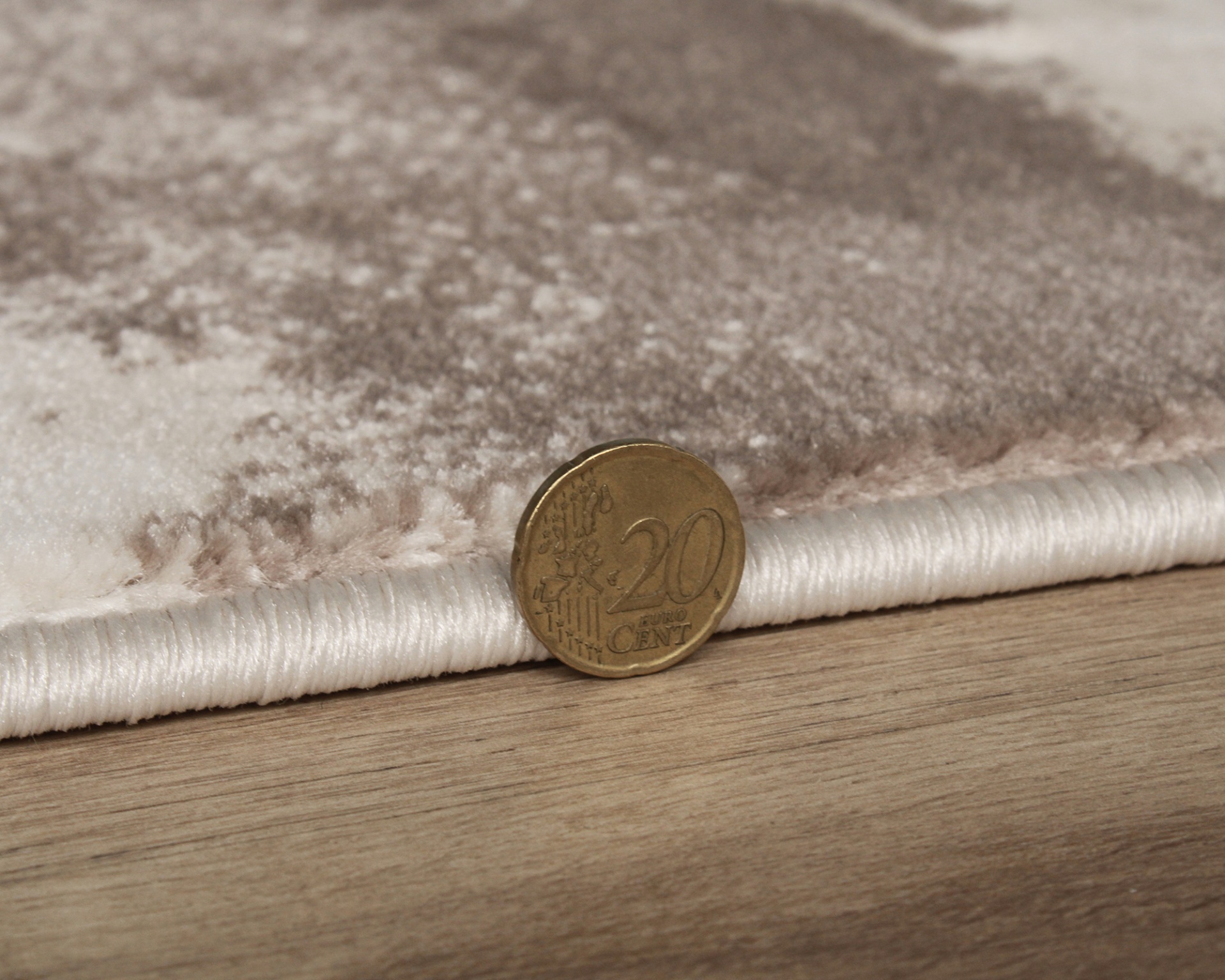 Tecido bege com padrão castanho junto a moeda de 20 centavos de euro sobre madeira