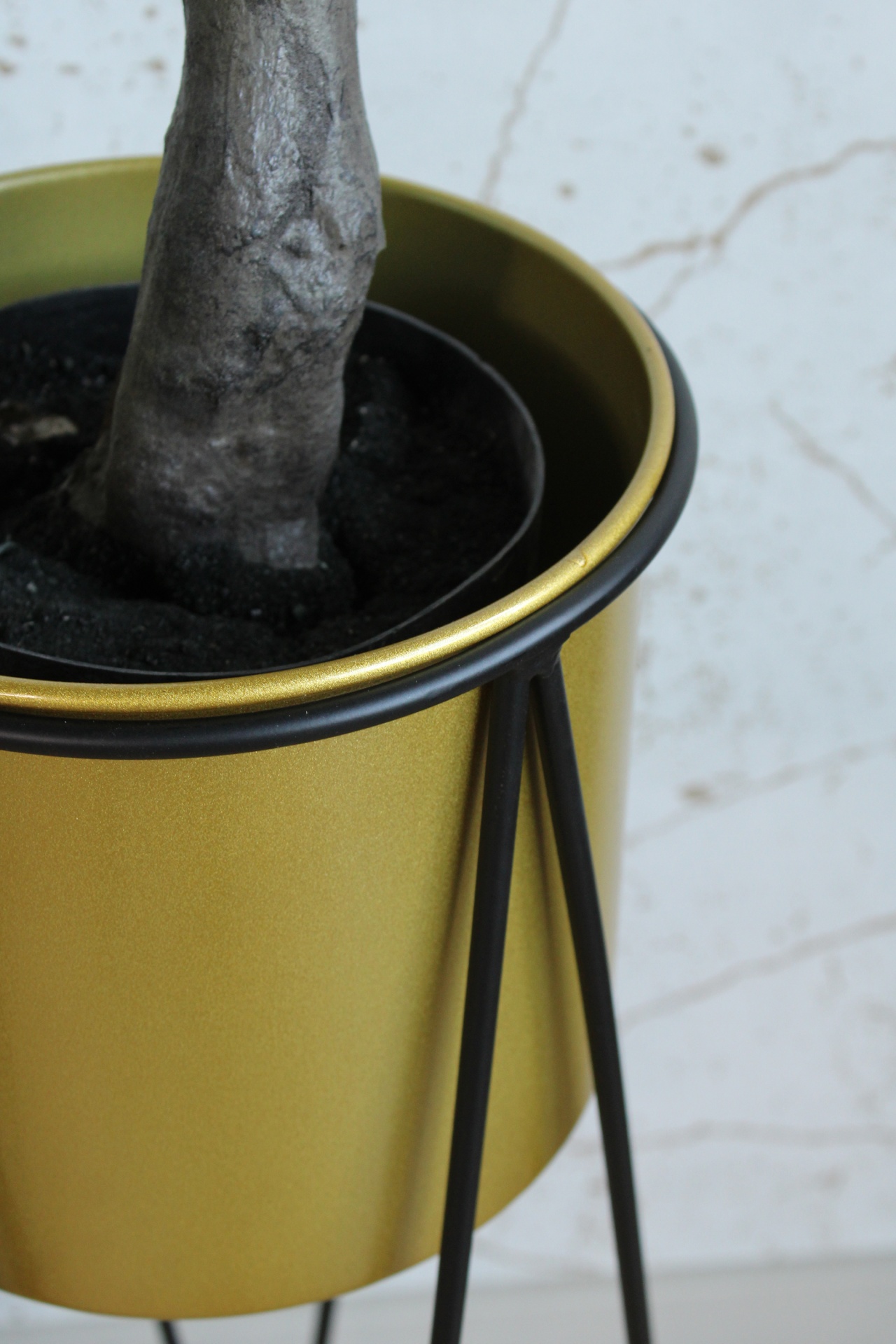 Vaso metálico dourado com suporte preto para planta e tronco