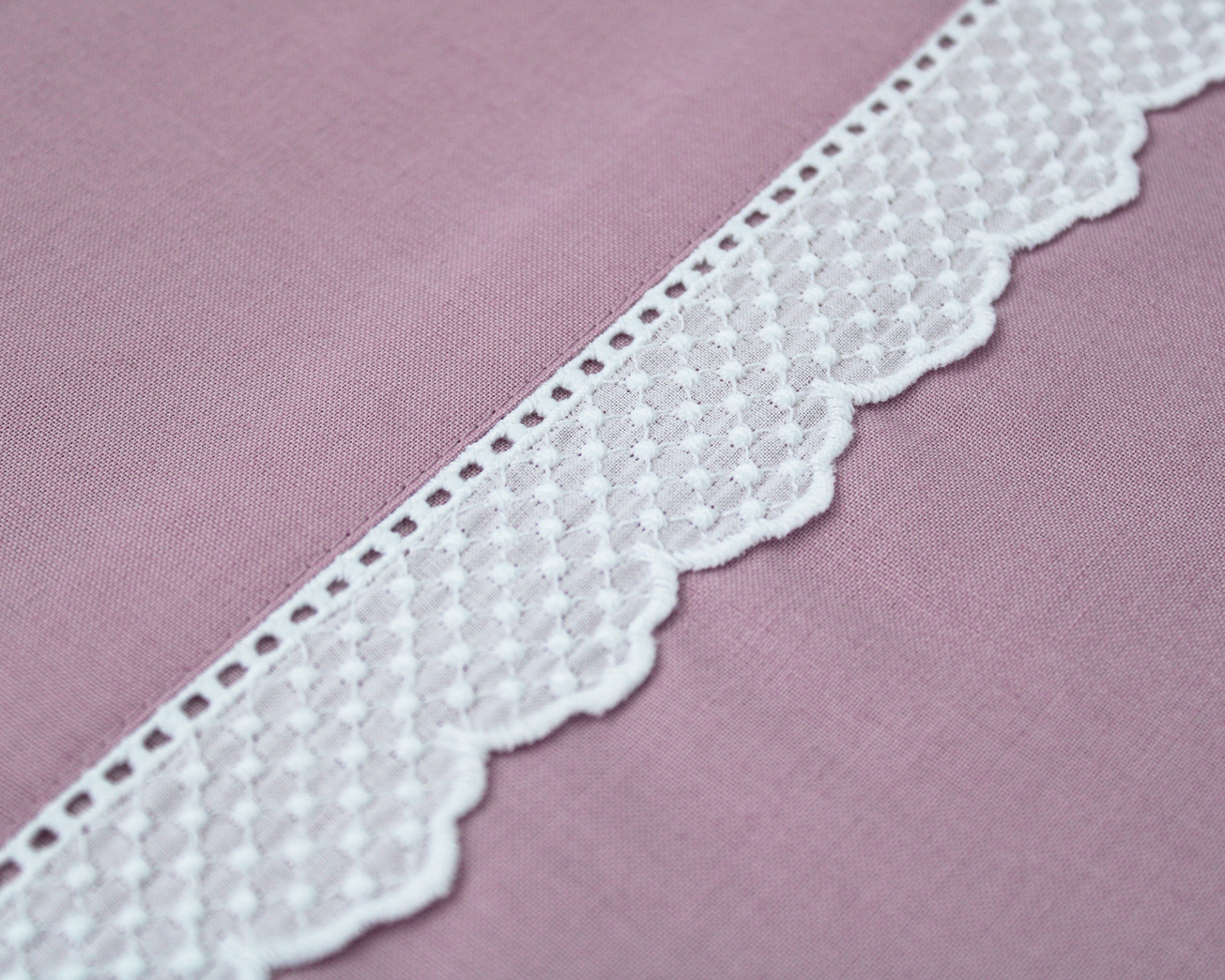 Tira de renda branca com padrão de pontos sobre tecido rosa claro