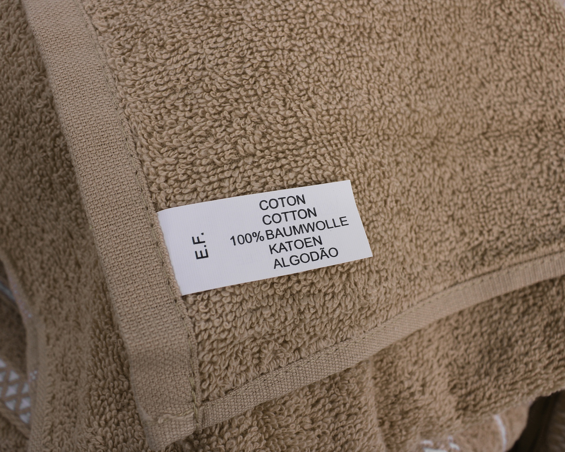 Toalha castanha de algodão com etiqueta com texto em várias línguas