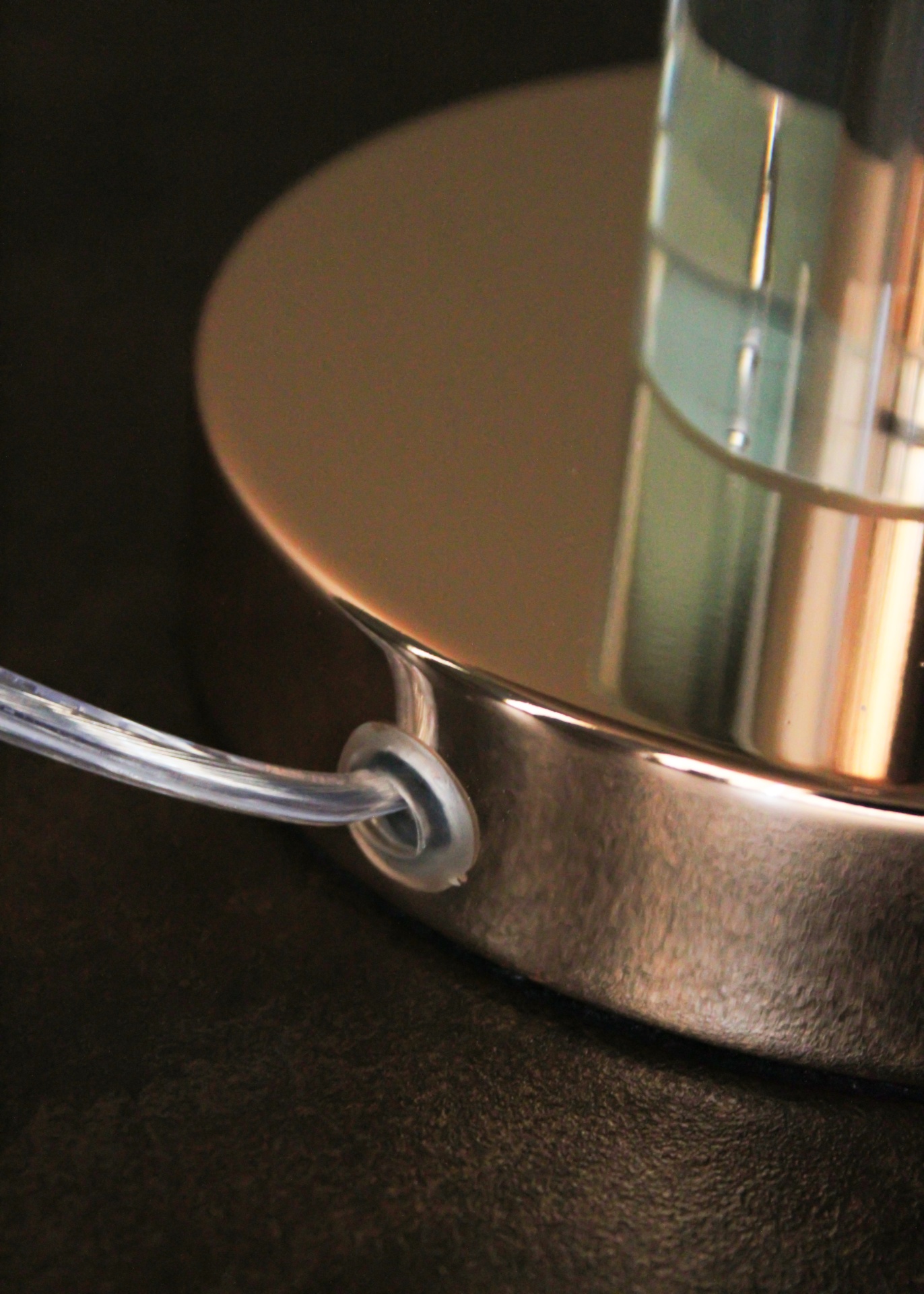 Base metálica prateada com fio transparente e borracha sobre superfície preta