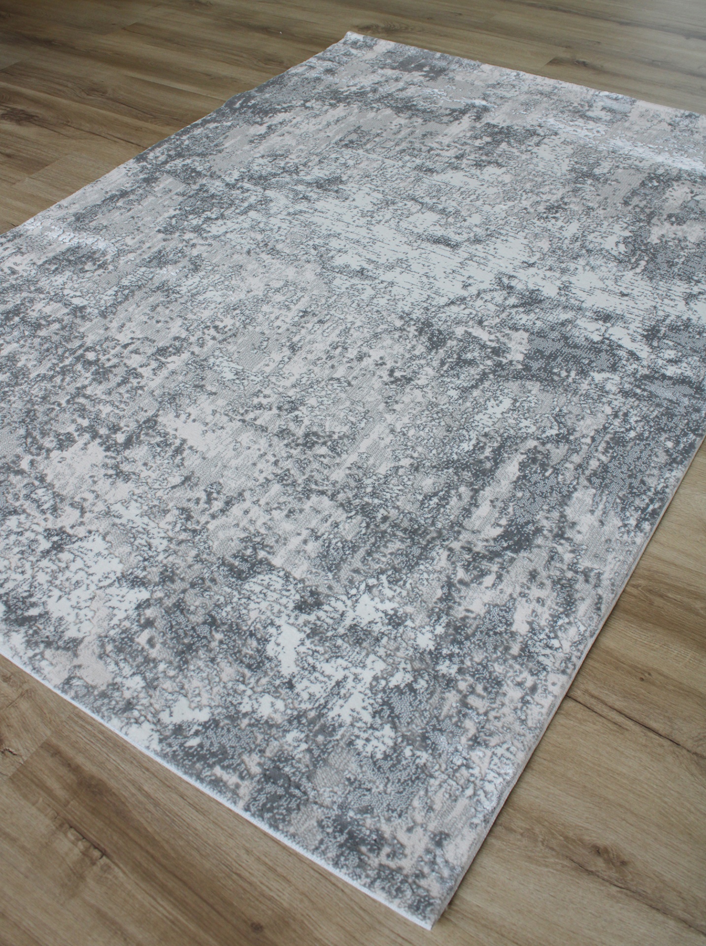 Tapete cinza e branco com padrão abstrato sobre chão de madeira