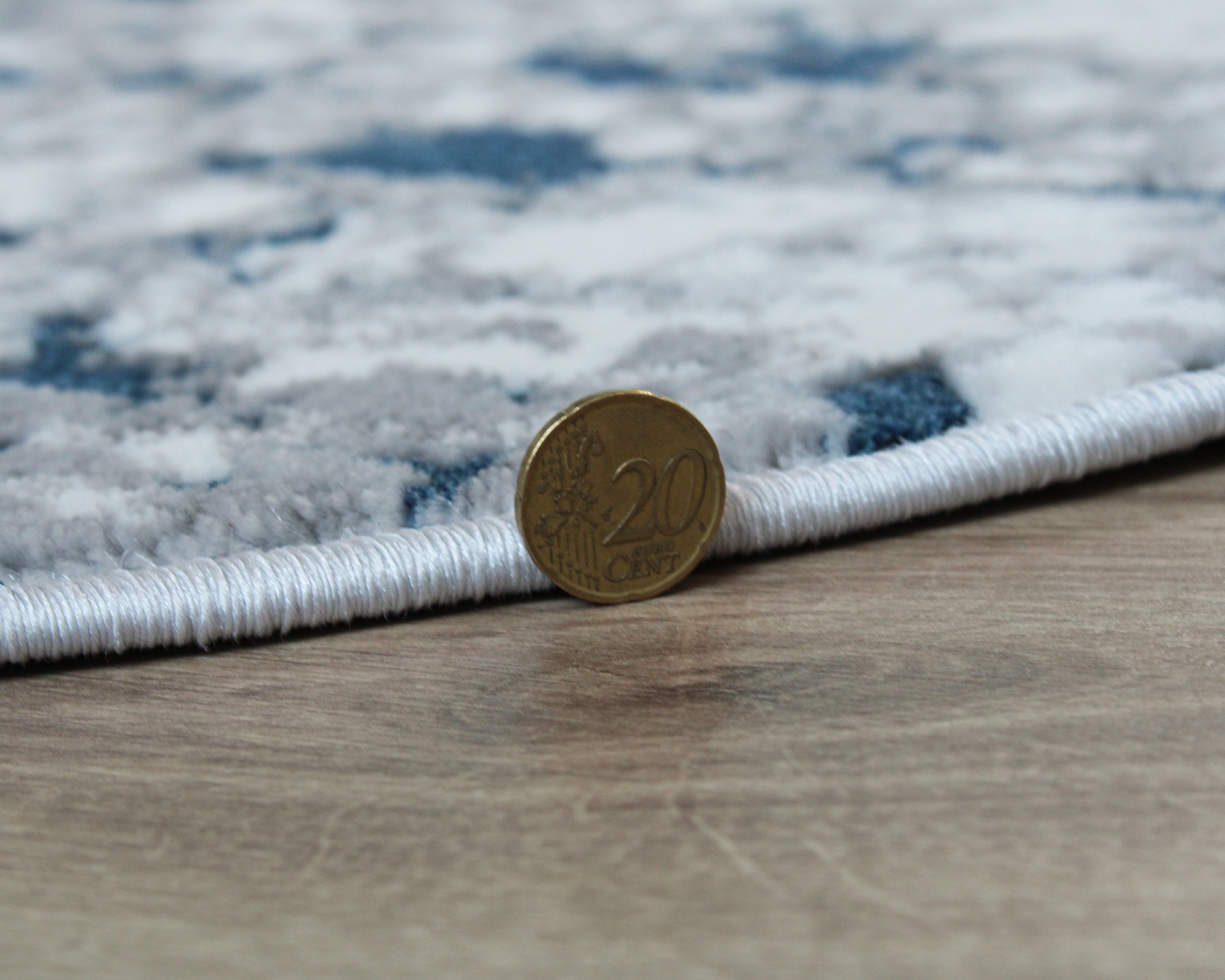 Tapete cinza, azul e branco com bordas brancas e moeda de 20 cêntimos sobre pavimento madeira