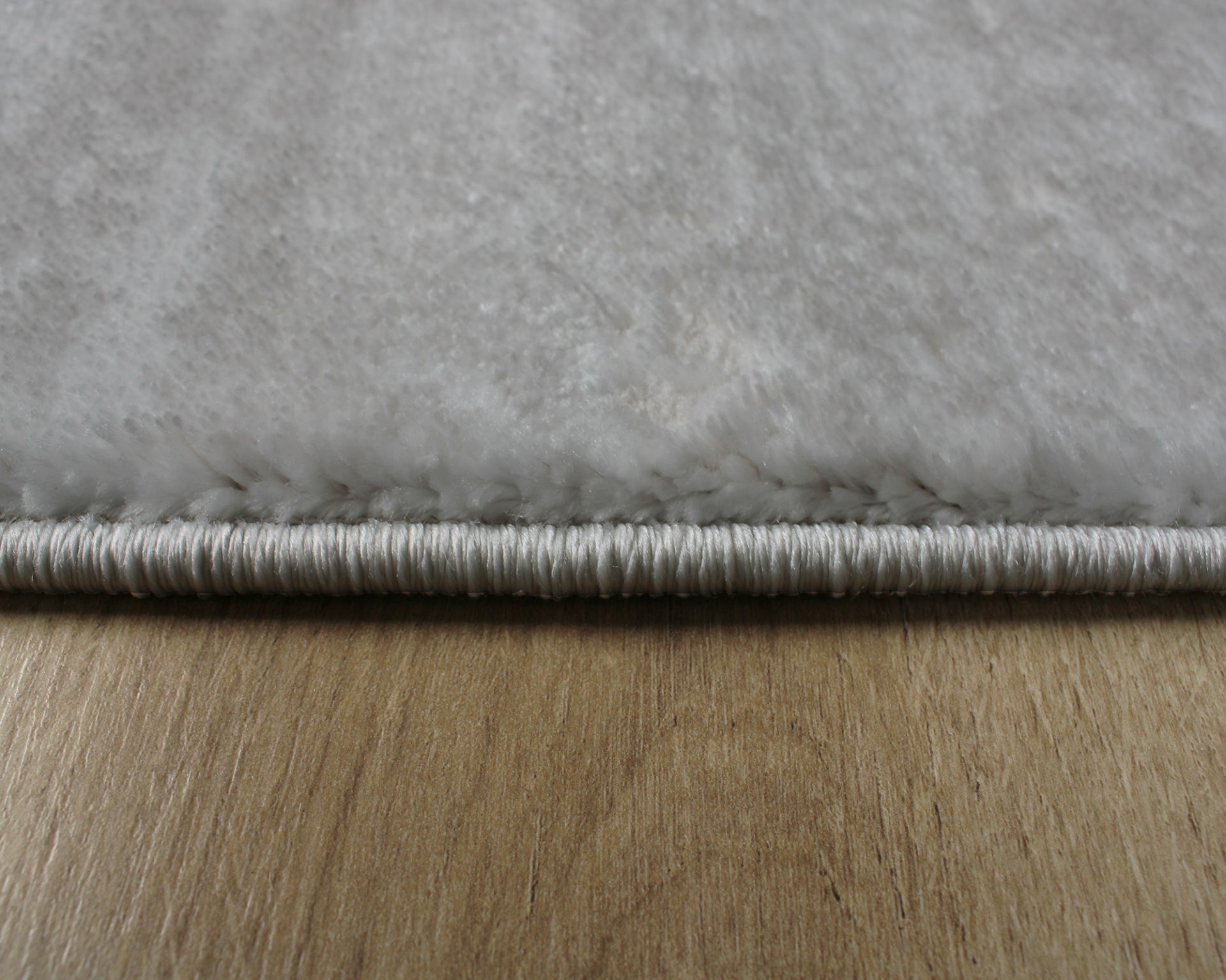 Tapete branco felpudo com borda e costura sobre chão de madeira