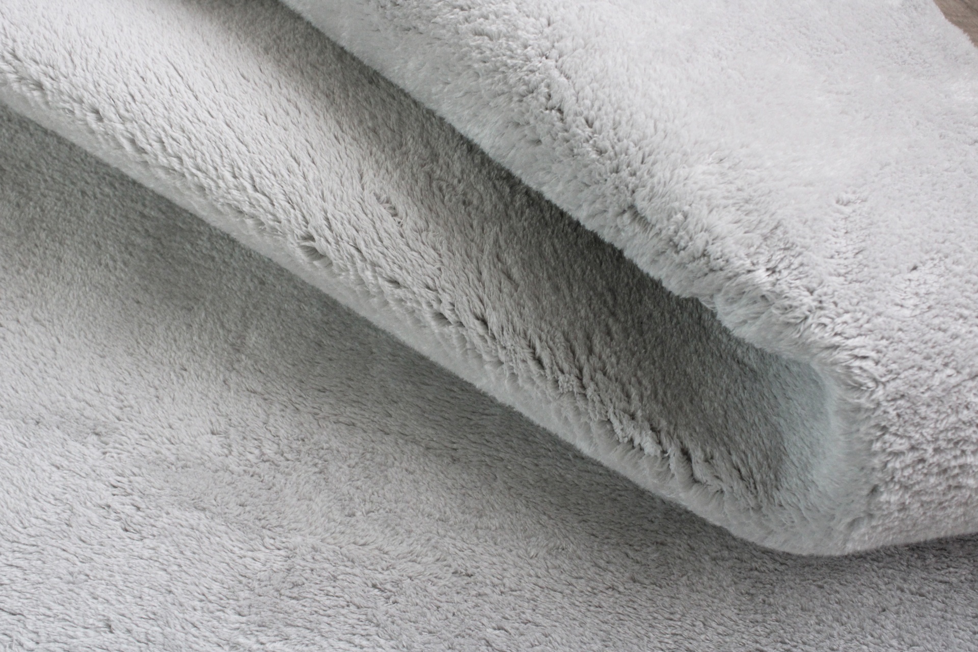 Tapete cinzento claro felpudo com textura macia e dobra visível