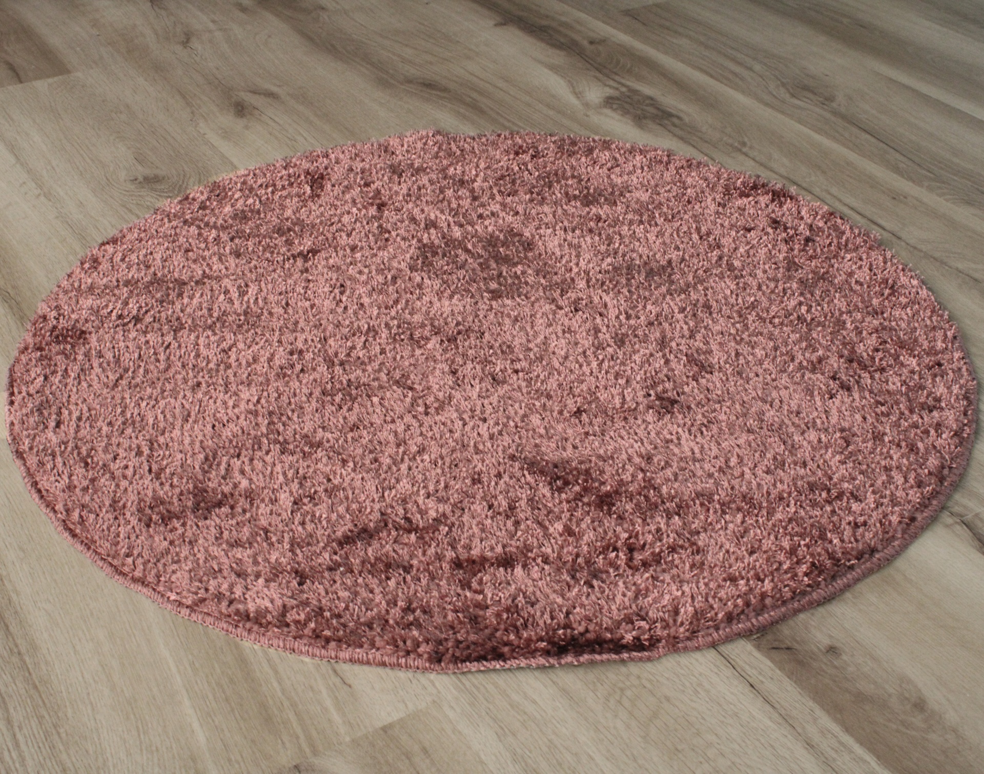 Tapete redondo rosa com pelo alto sobre chão de madeira clara