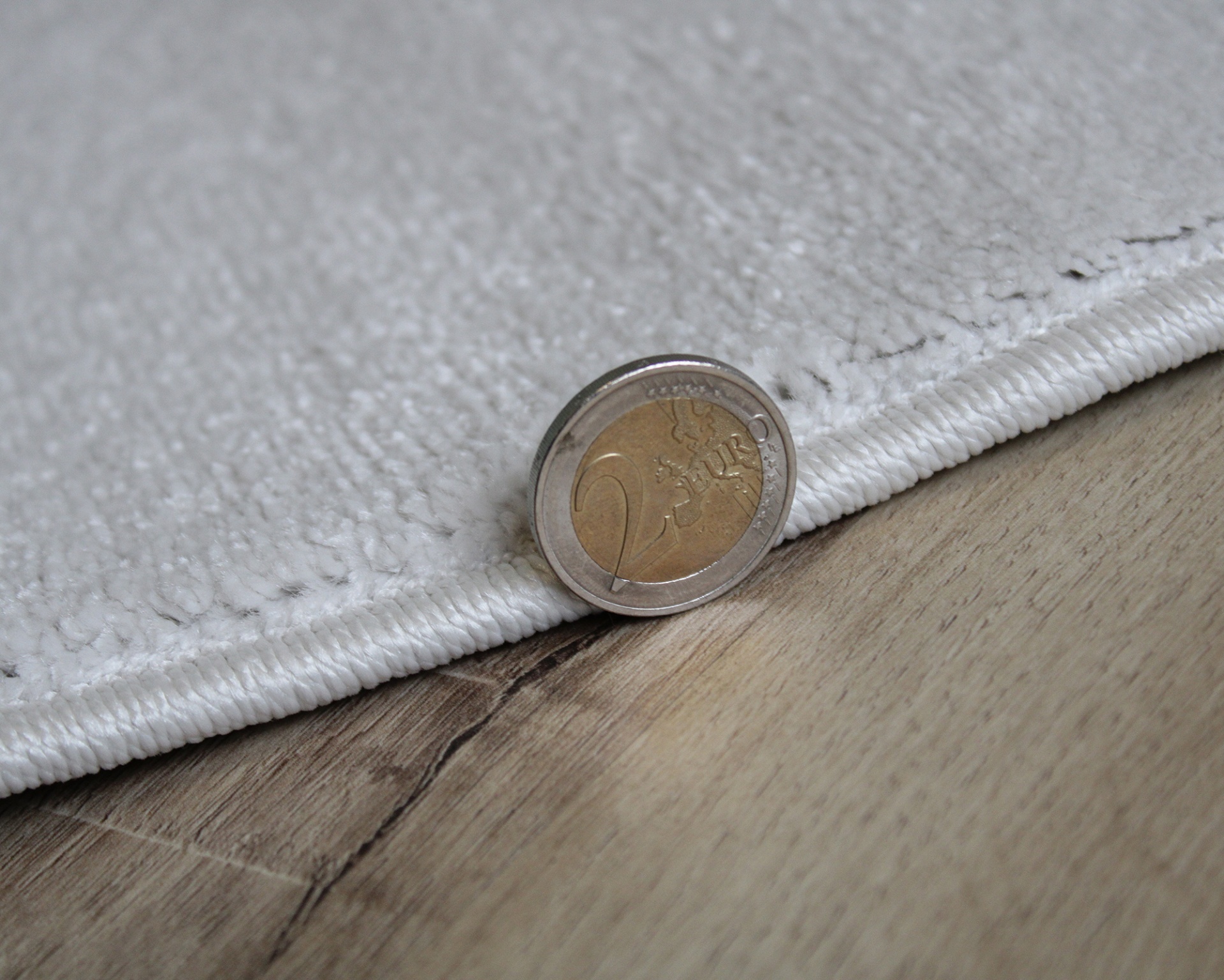 Tapete branco macio com moeda de 2 euros na borda sobre chão de madeira clara