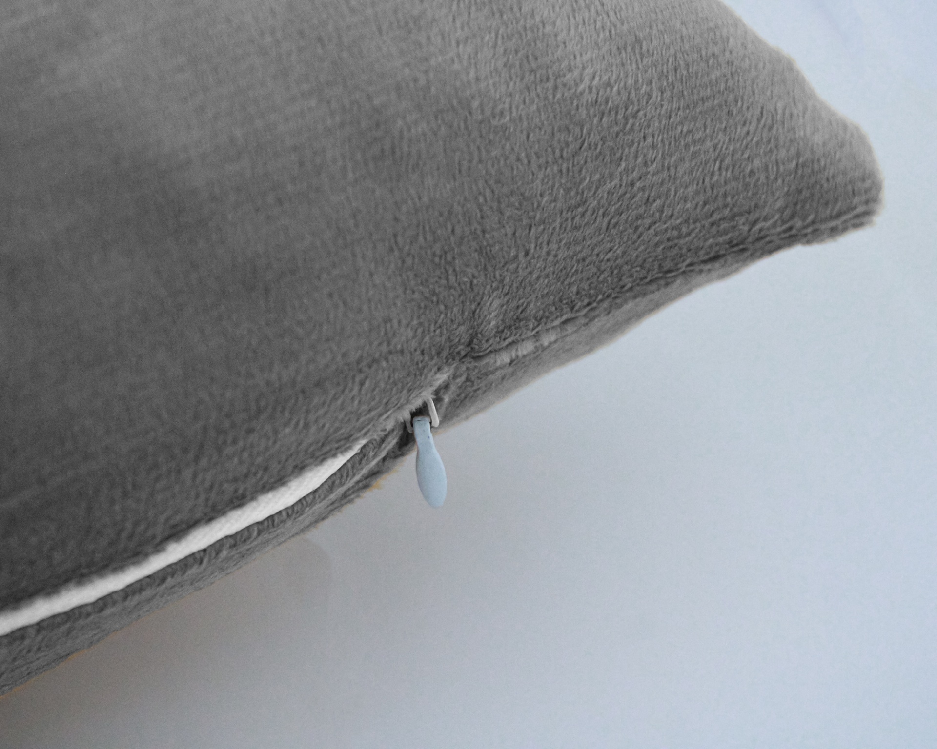 Almofada cinzenta com fecho de correr branco visível na lateral