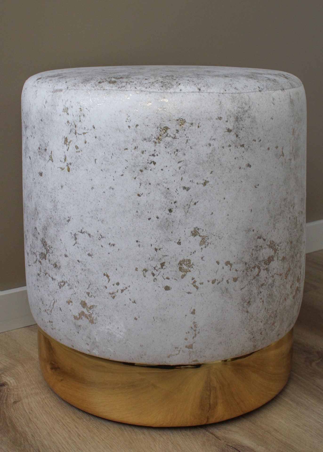 Pufe redondo branco com base dourada sobre chão de madeira