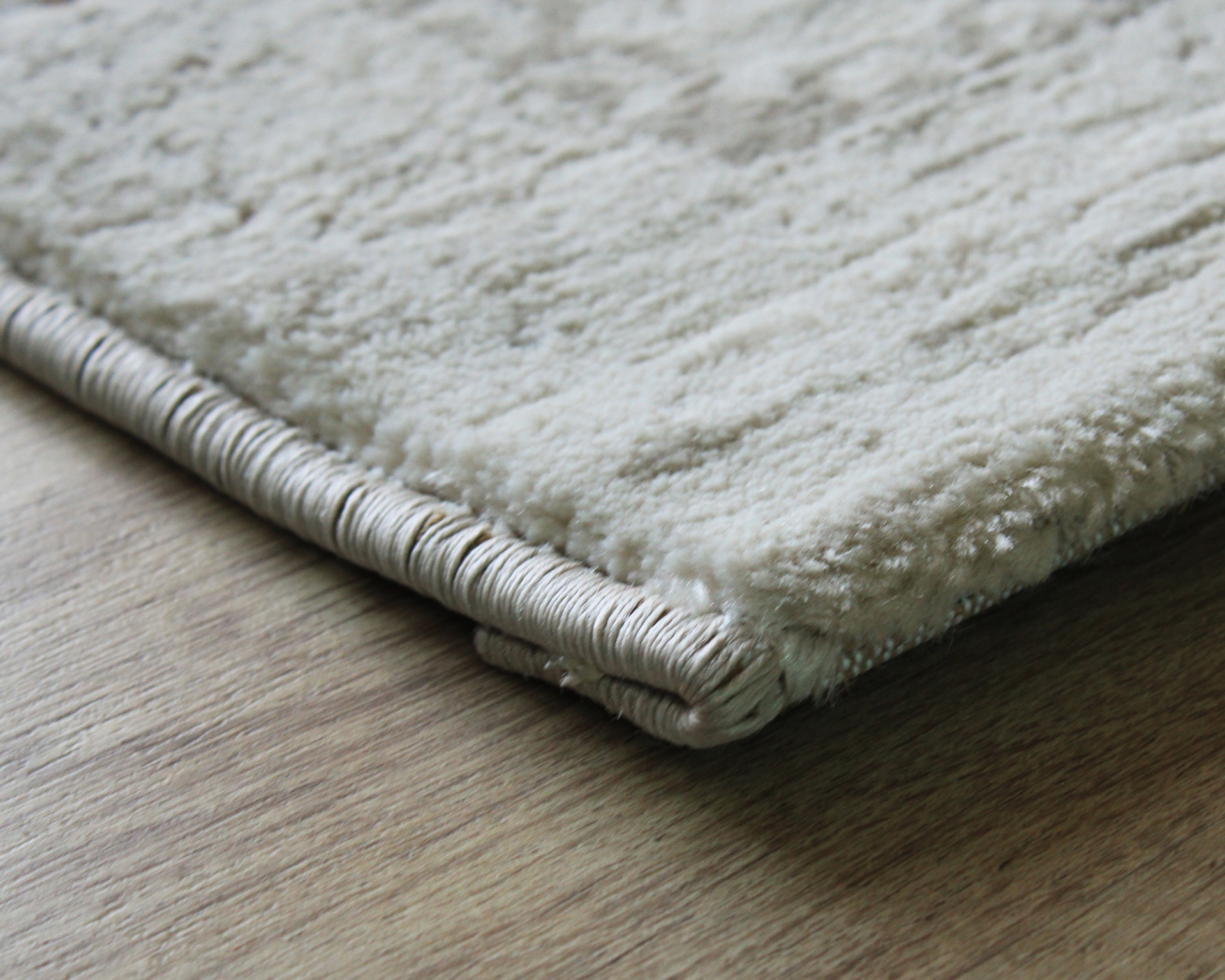 Tapete branco de pelo curto com borda revestida em chão de madeira clara