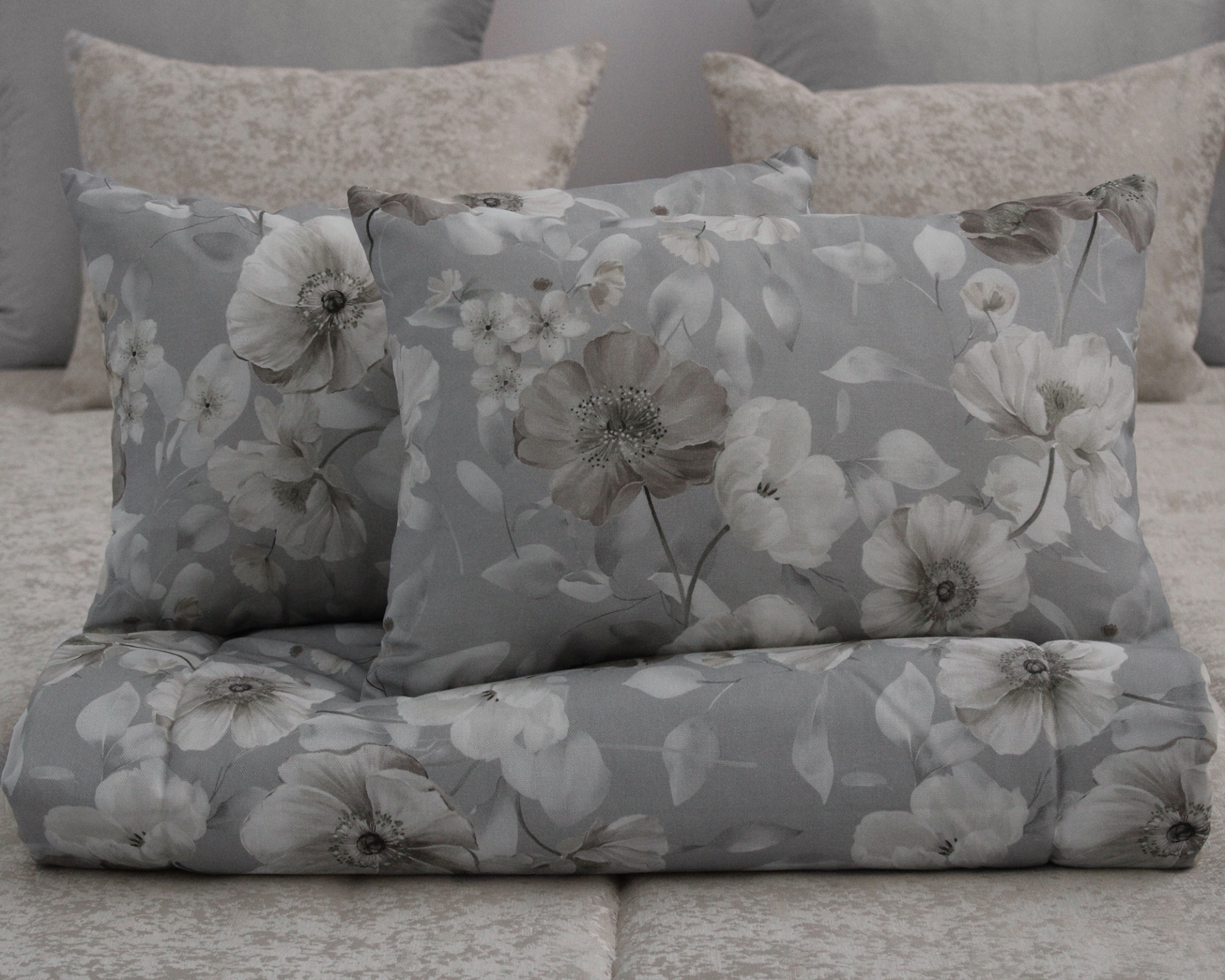 Almofadas e edredão cinzentos com padrão floral sobre cama