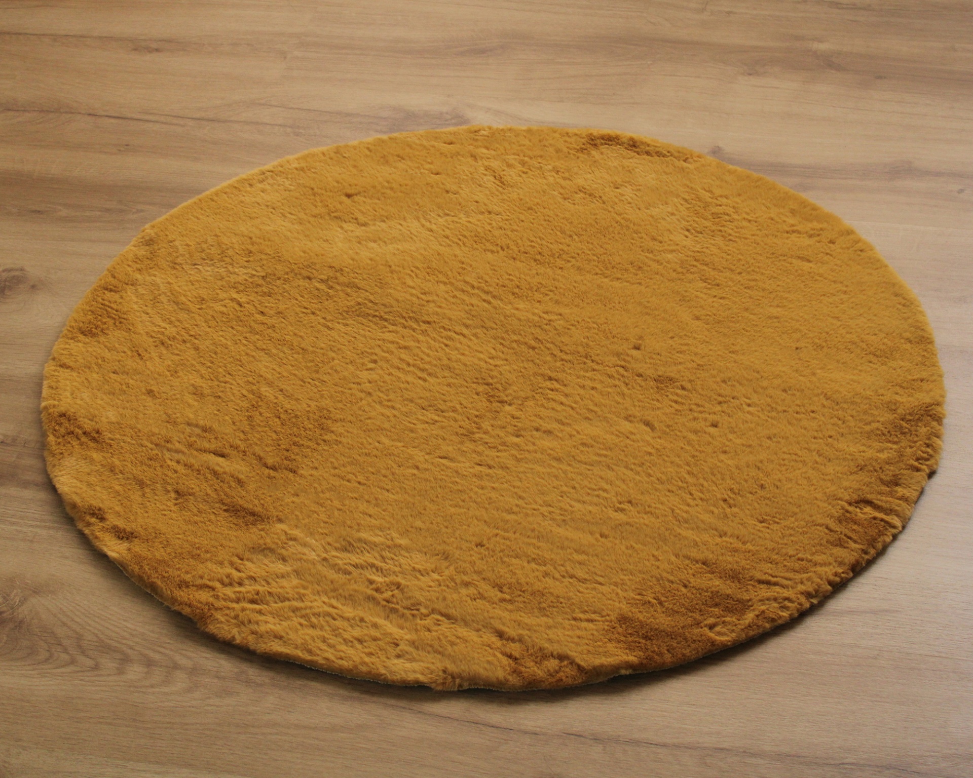 Tapete redondo amarelo mostarda felpudo sobre chão de madeira clara