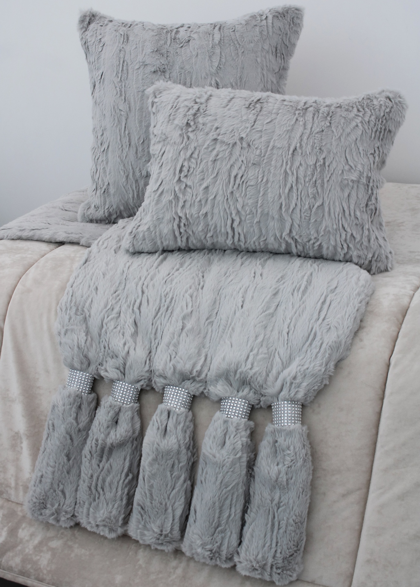 Conjunto de almofadas e manta cinzentas felpudas com franjas brilhantes sobre cama clara