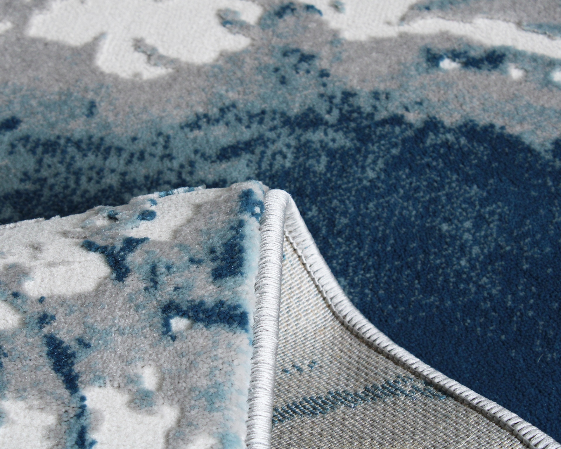 Tapete azul, cinza e branco com padrão abstrato e bordas cosidas