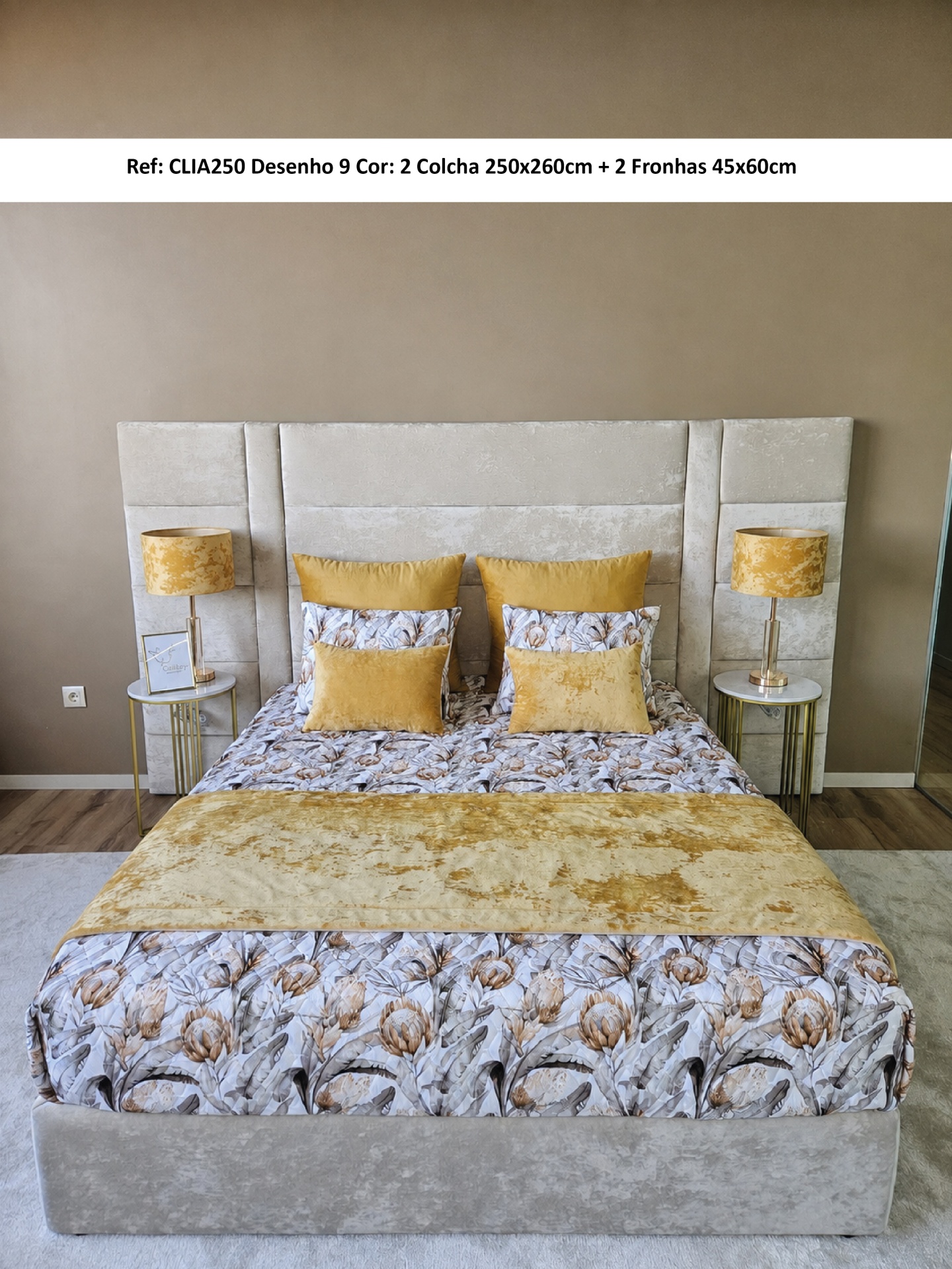 Cama estofada cinza claro com roupa de cama floral bege e castanho, almofadas amarelas, duas mesas de cabeceira com lâmpadas amarelas