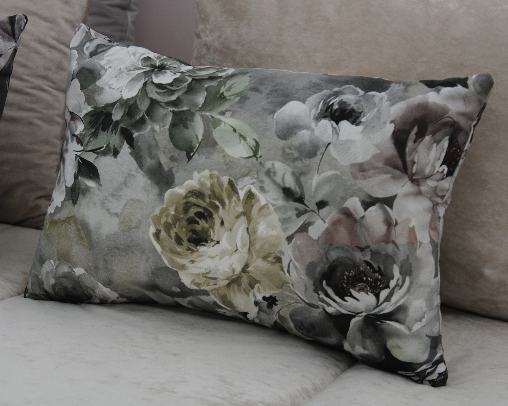 Almofada retangular estampada com flores em tons neutros sobre sofá bege