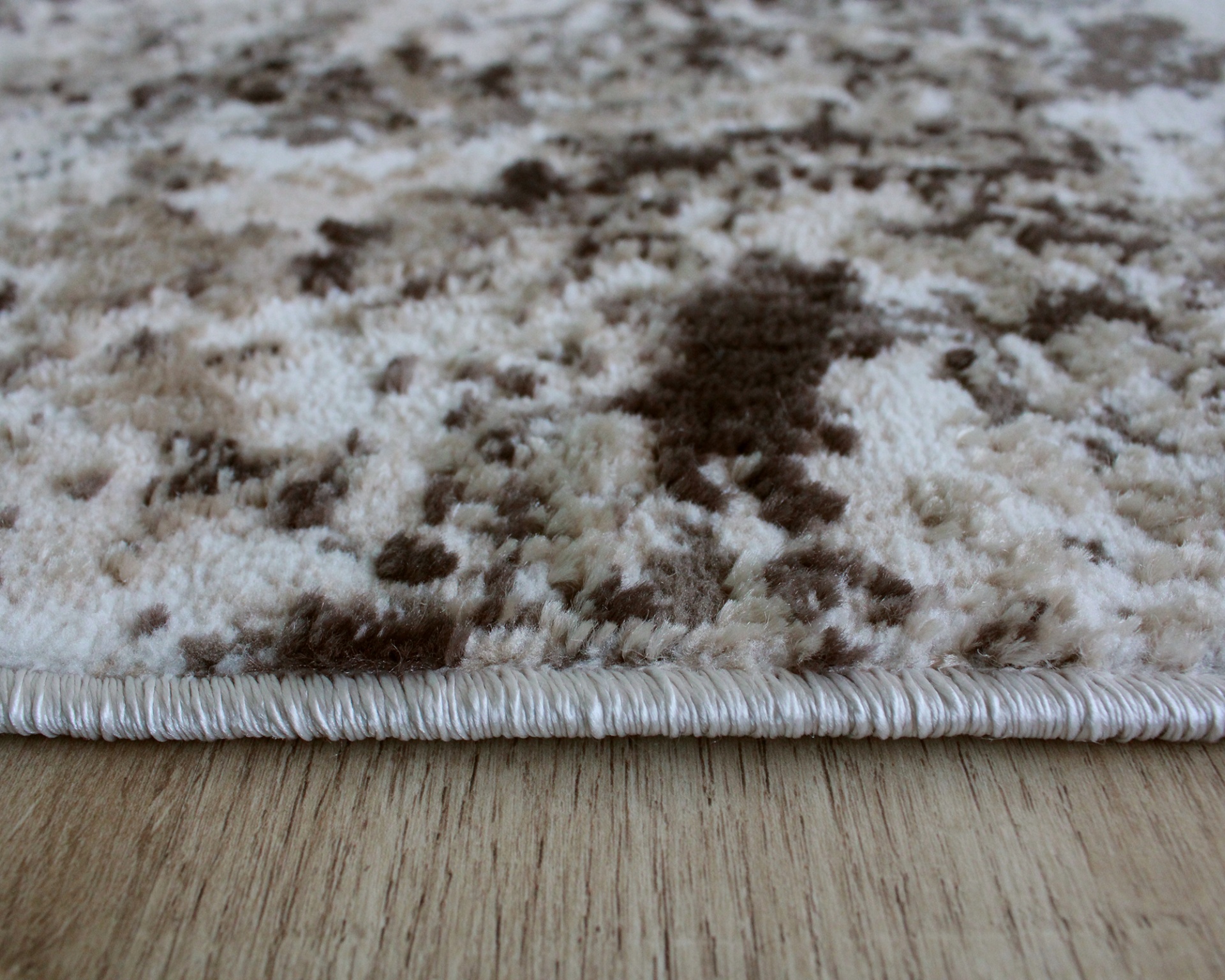 Tapete felpudo marmoreado castanho e bege com borda costurada sobre piso de madeira