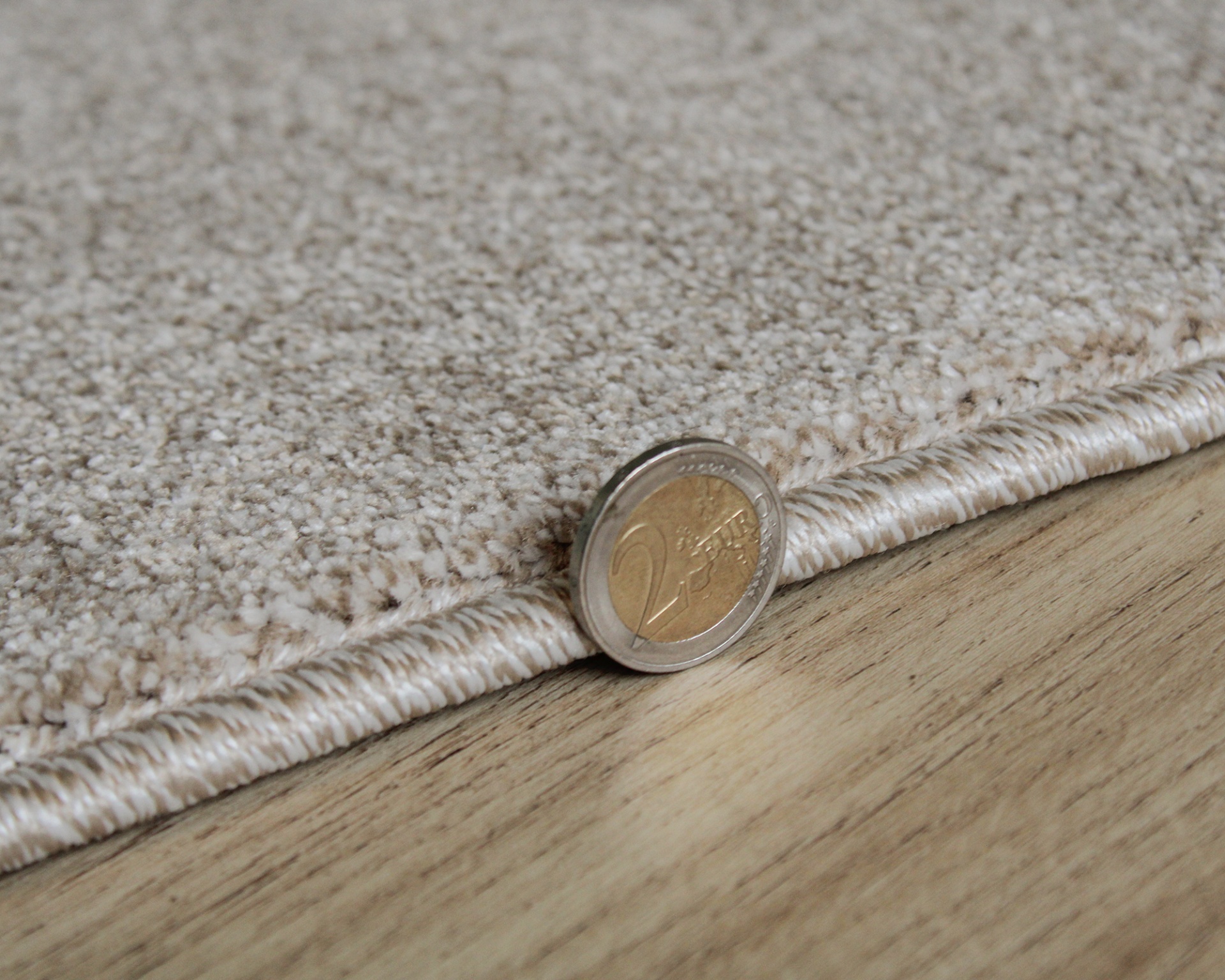 Tapete bege claro com textura felpuda e borda resistente sobre chão de madeira clara e moeda de 2 euros à frente