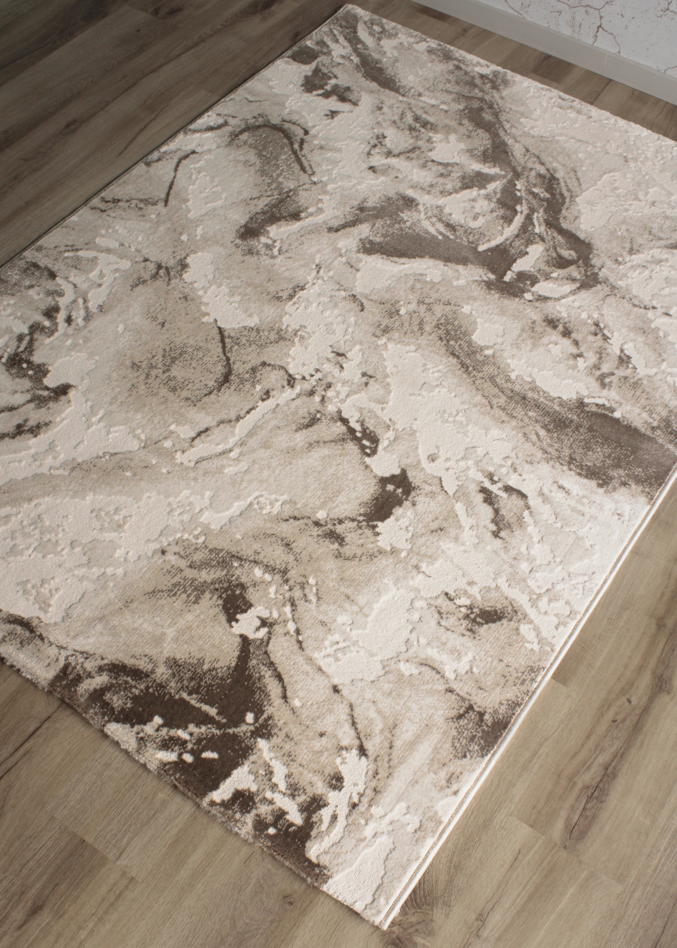 Tapete retangular com padrão abstrato em tons de bege e castanho sobre chão de madeira clara