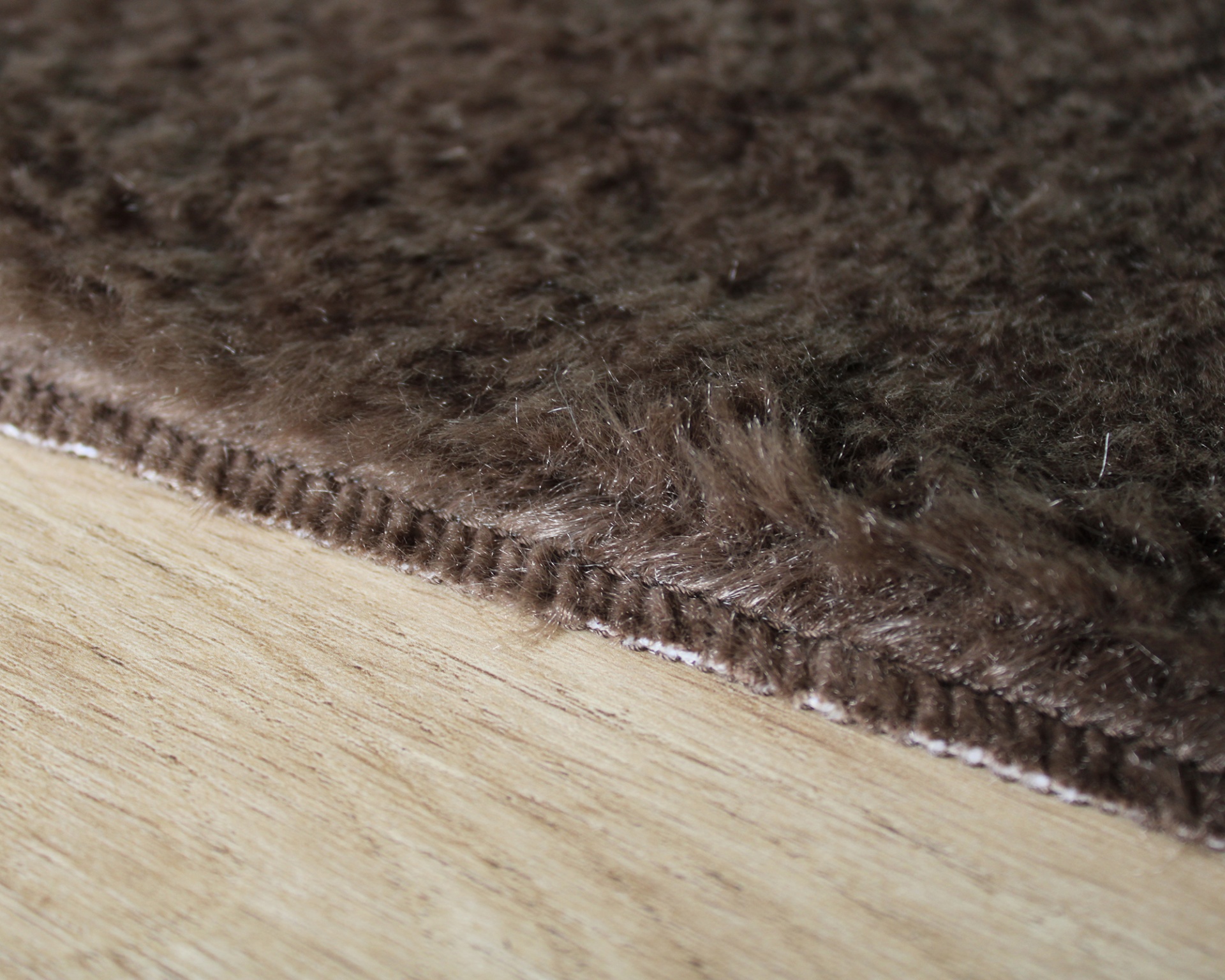 tapete castanho escuro com borda costurada sobre piso de madeira clara