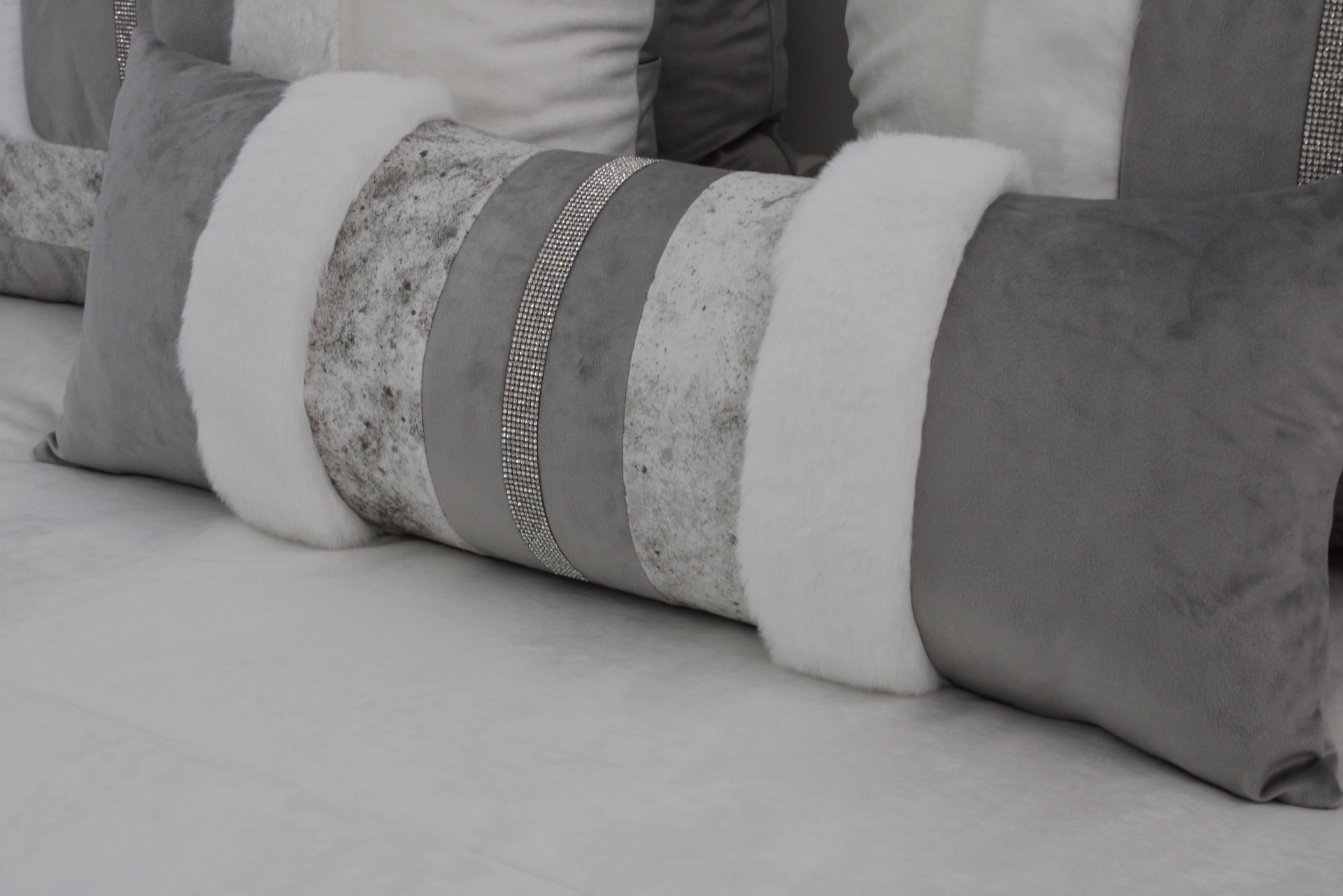 Almofada retangular cinza com detalhes em tecido branco e faixas decorativas cinzentas