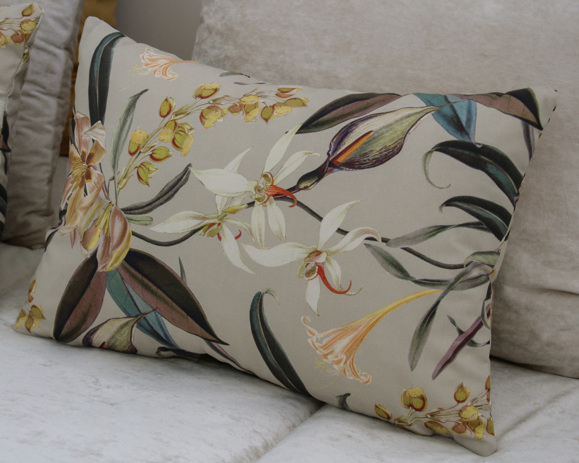 Almofada retangular cinza com padrão floral colorido num sofá creme.