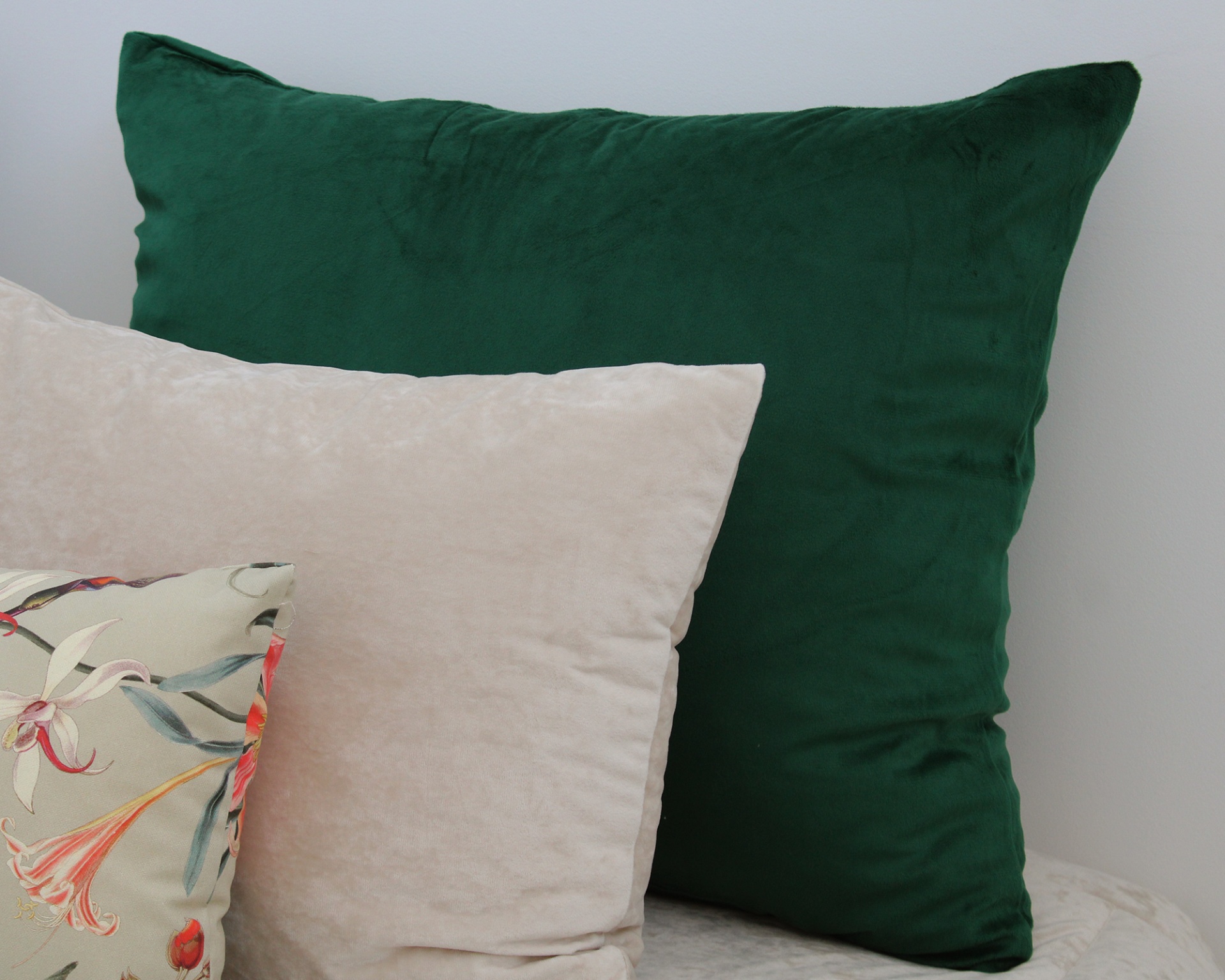 Três almofadas com tecidos verde, bege e padrão floral colocadas juntas
