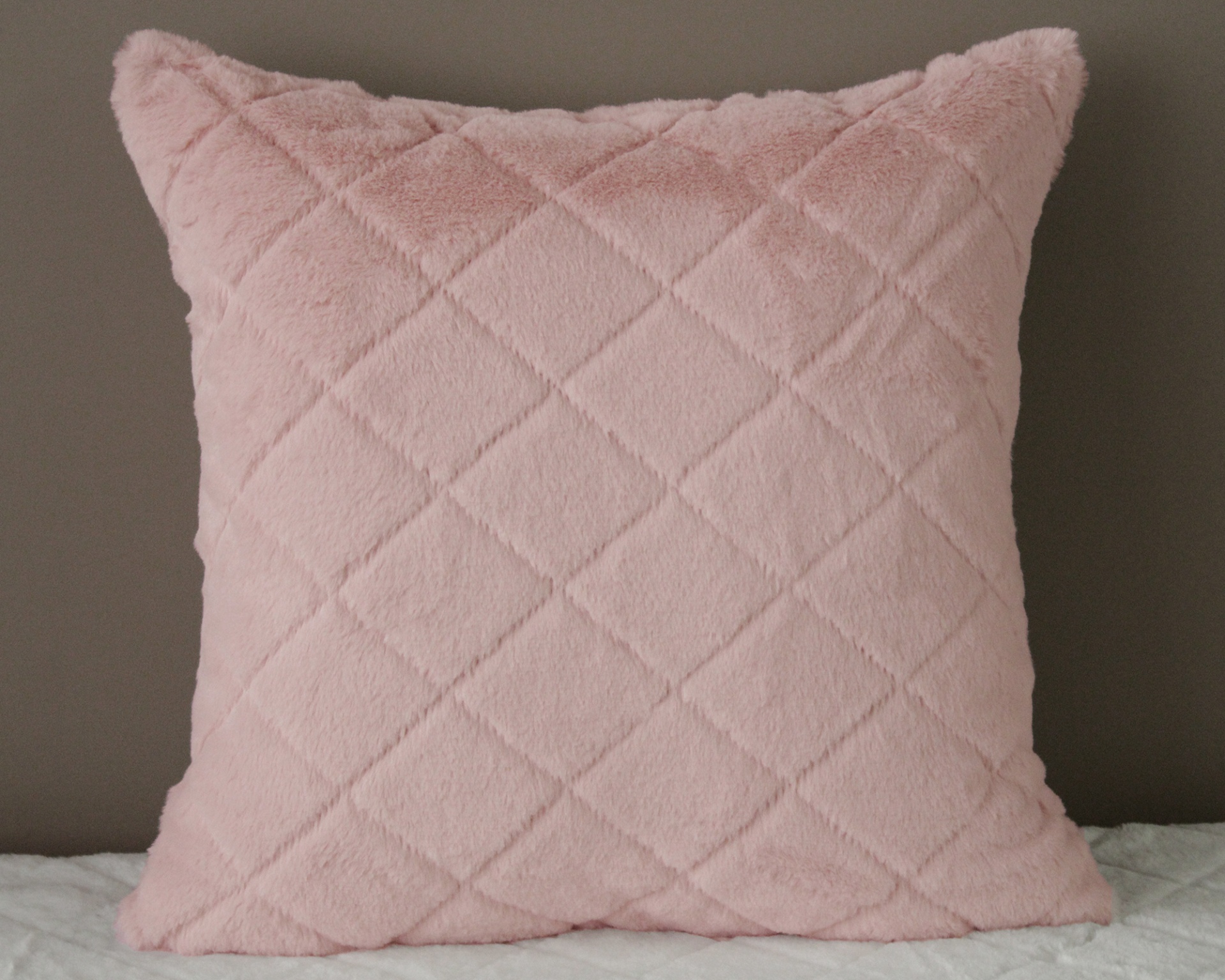 Almofada rosa com padrão em relevo sobre superfície branca e parede cinza