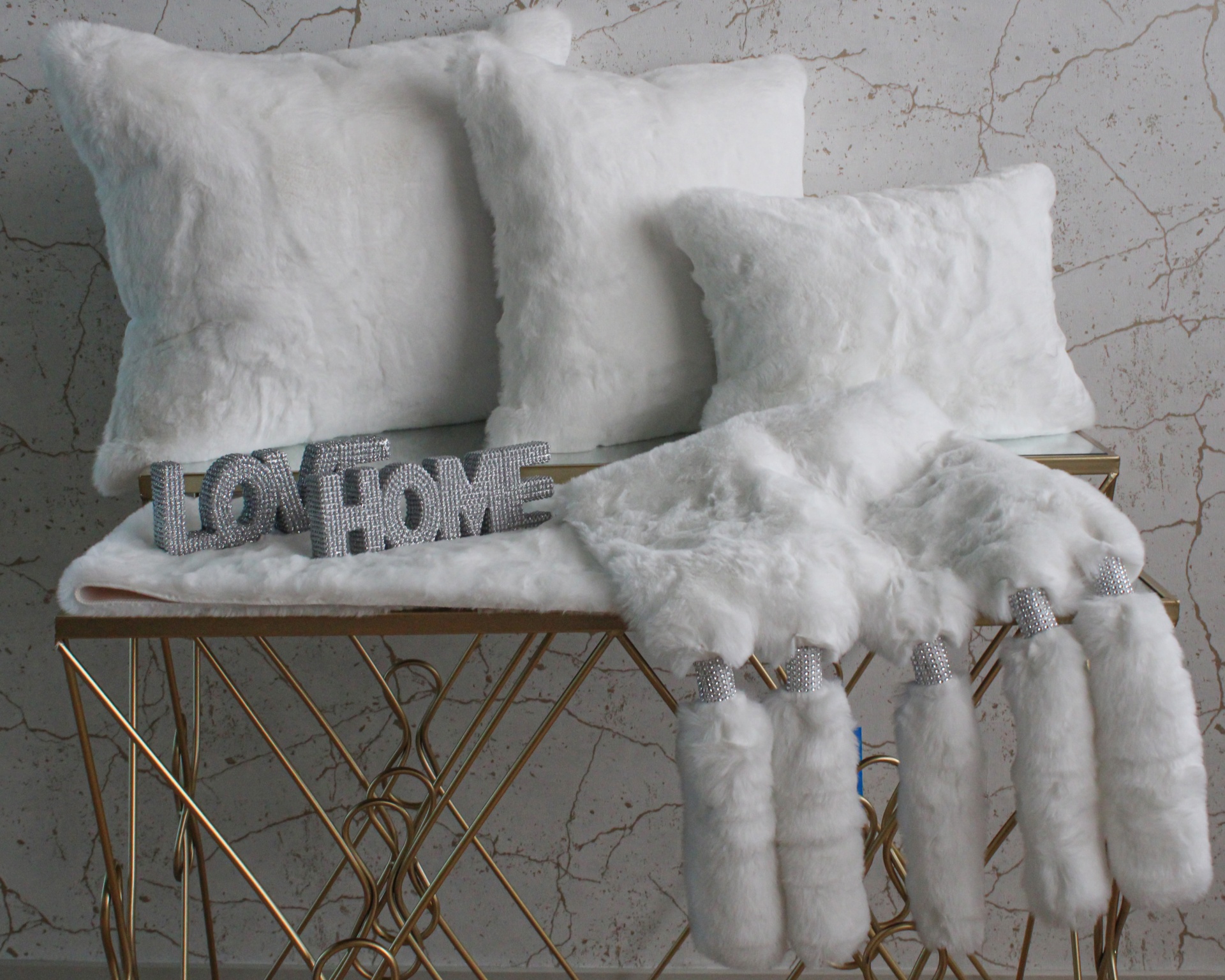 Almofadas e manta brancas felpudas sobre banco dourado com texto decorativo HOME