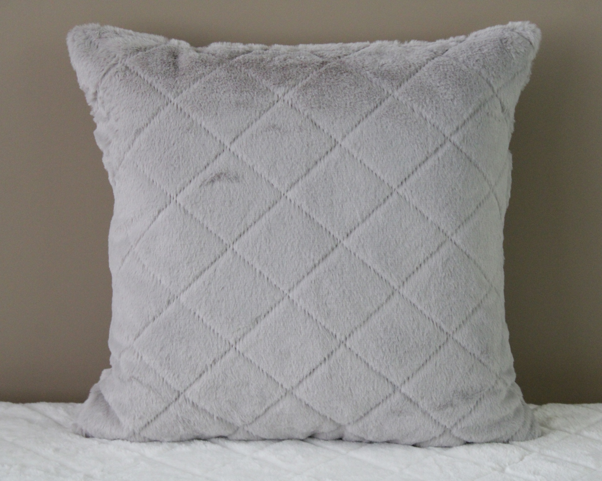 Almofada cinza claro com padrão em losangos felpuda sobre superfície branca