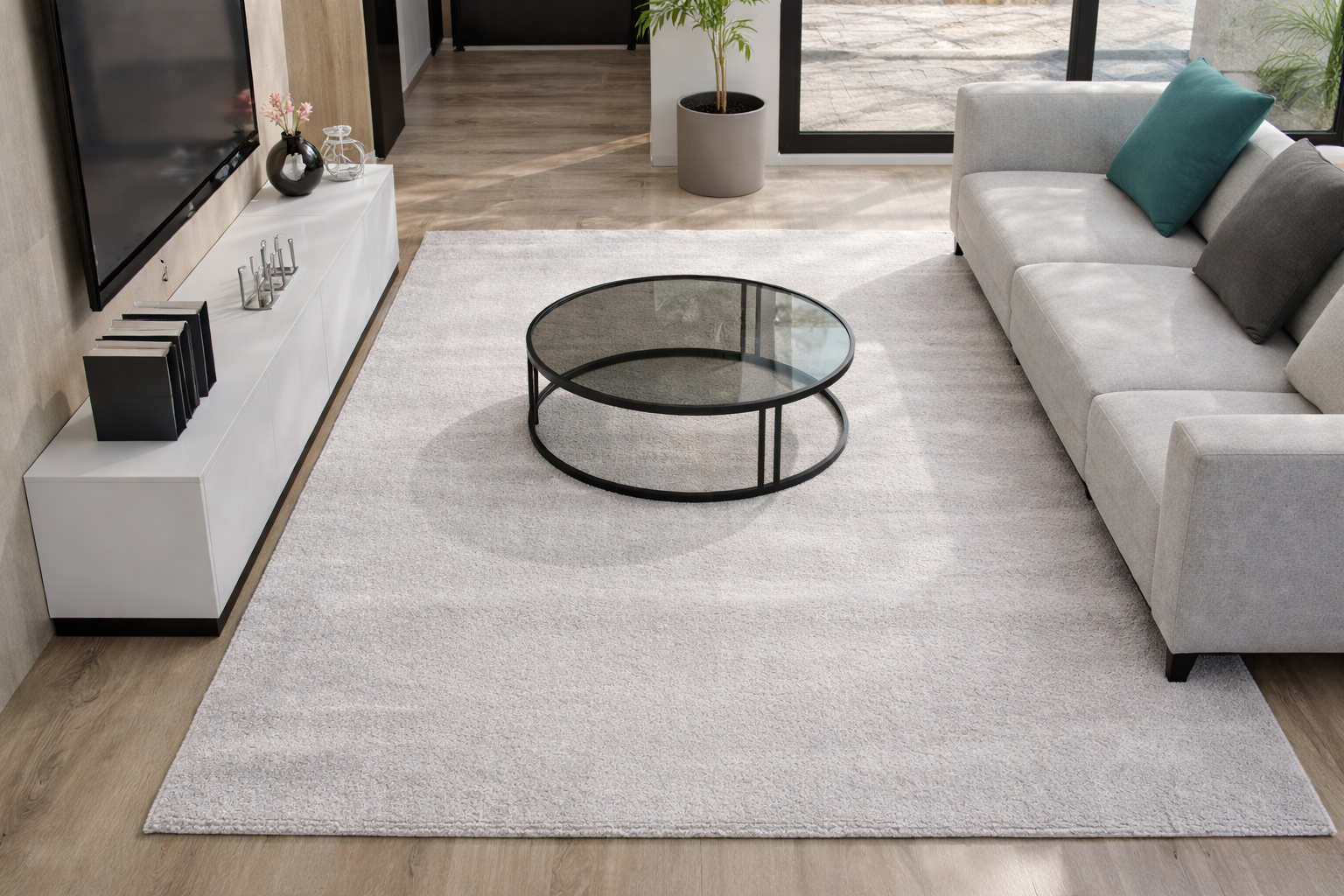 Sala de estar moderna com sofá cinza claro, mesa de centro redonda de vidro, tapete branco e móvel branco