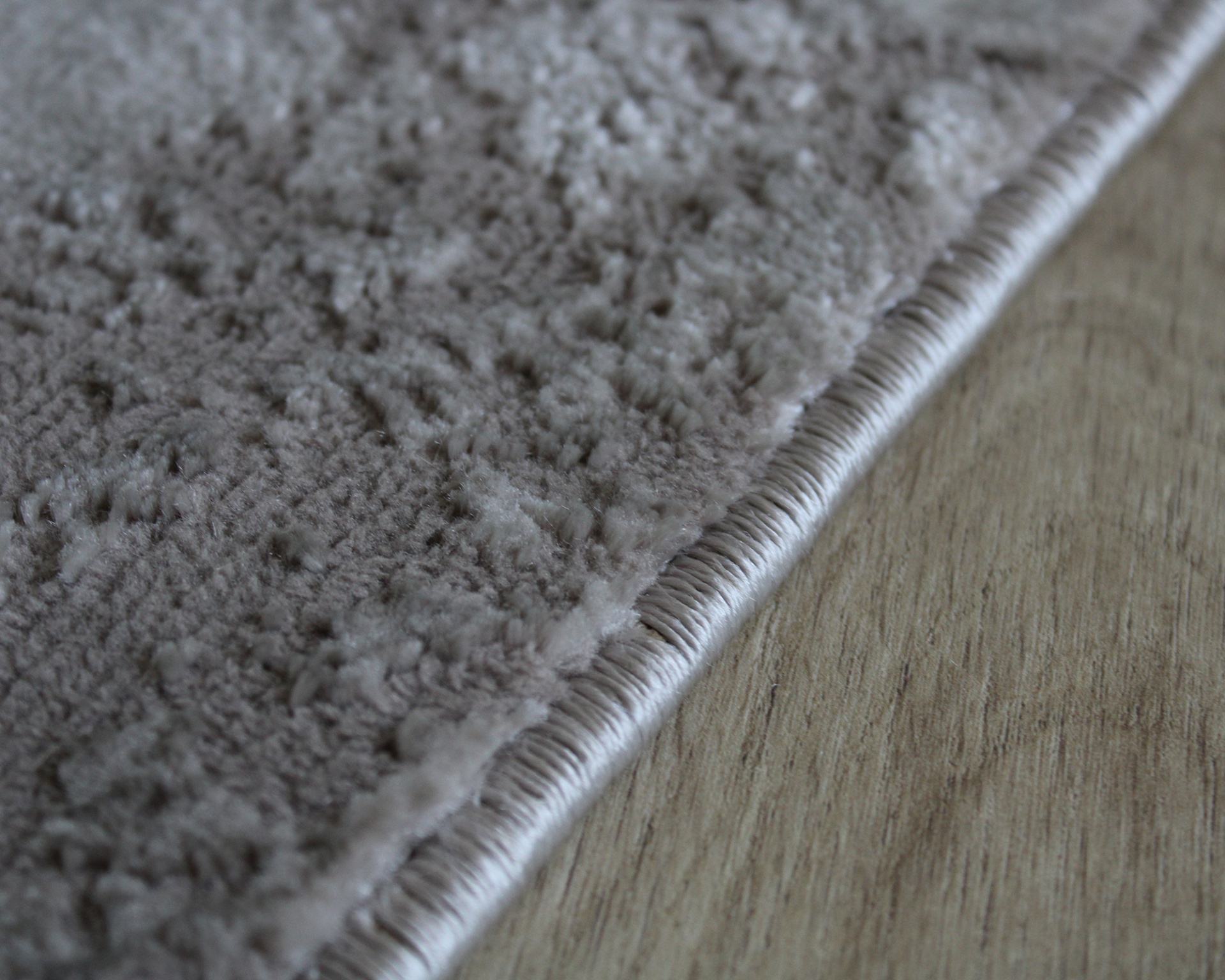 Tapete cinza claro com borda costurada em chão de madeira