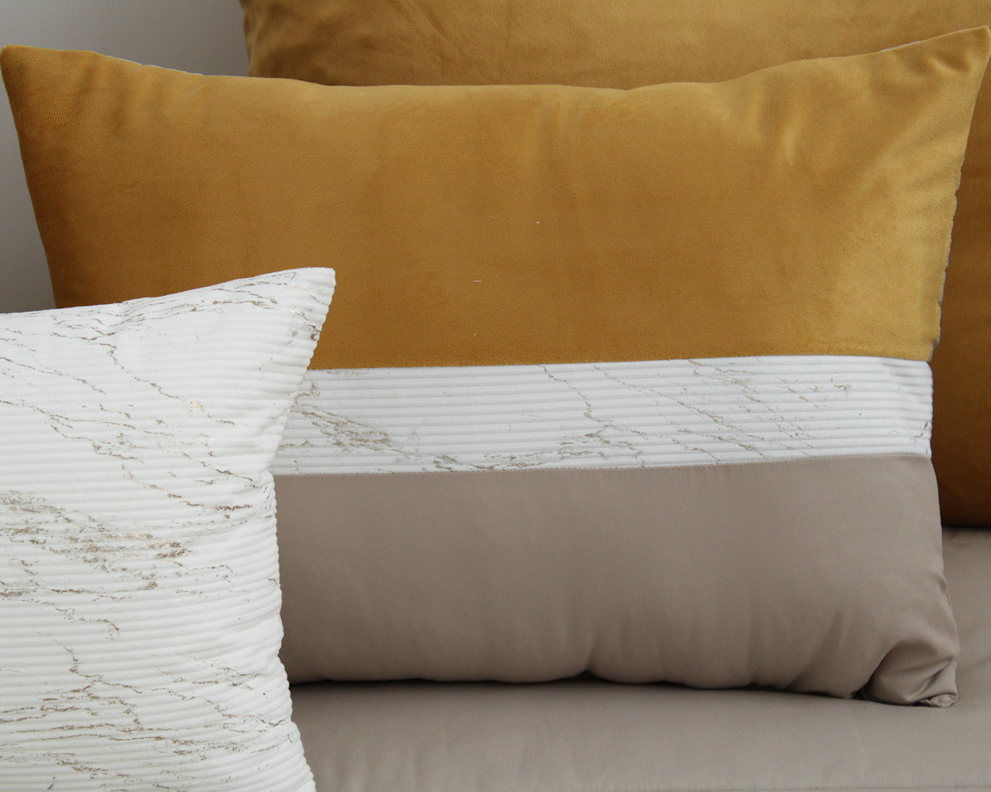 Almofadas amarelo-mostarda e retangular branco, cinza com padrão abstrato em sofá.